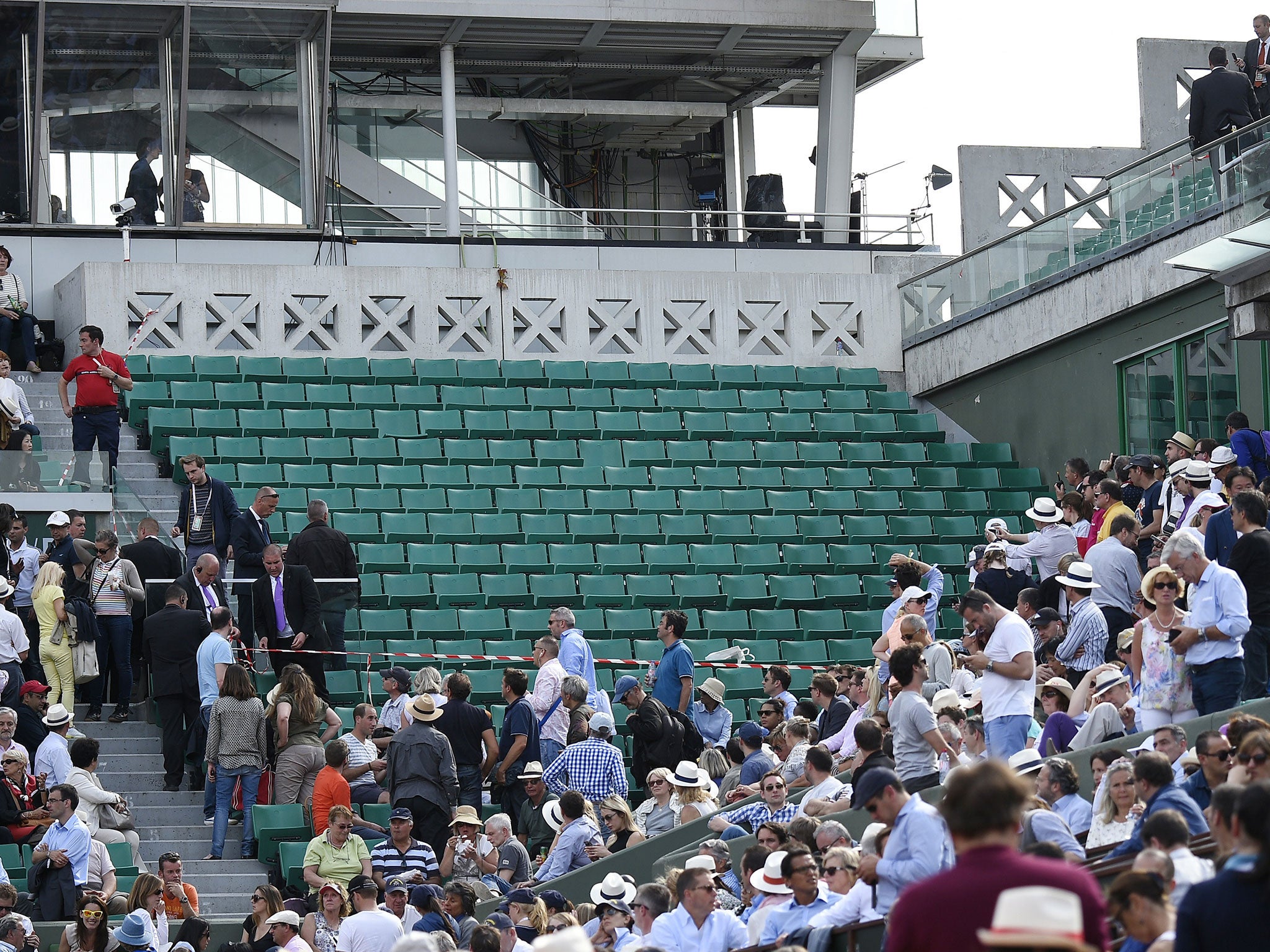 Members of security move spectators after a piece of the scoreboard above Court Philippe Chatrier was blown off in high winds