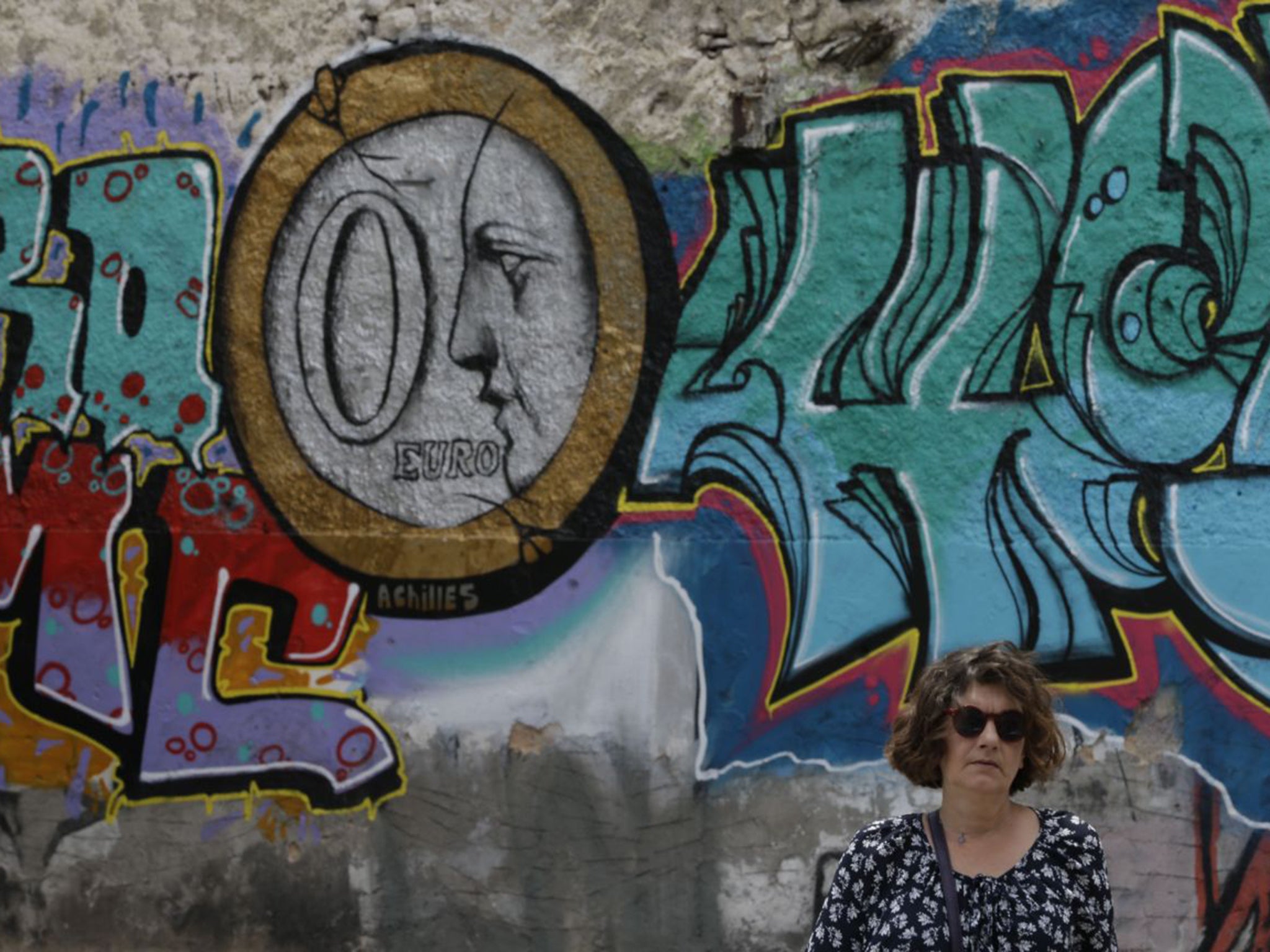 A woman stands in front of graffiti depicting a zero Euro coin in Athens. Fears are growing that a deal will not be reached to repay a first tranche of Greece’s debts to international lenders