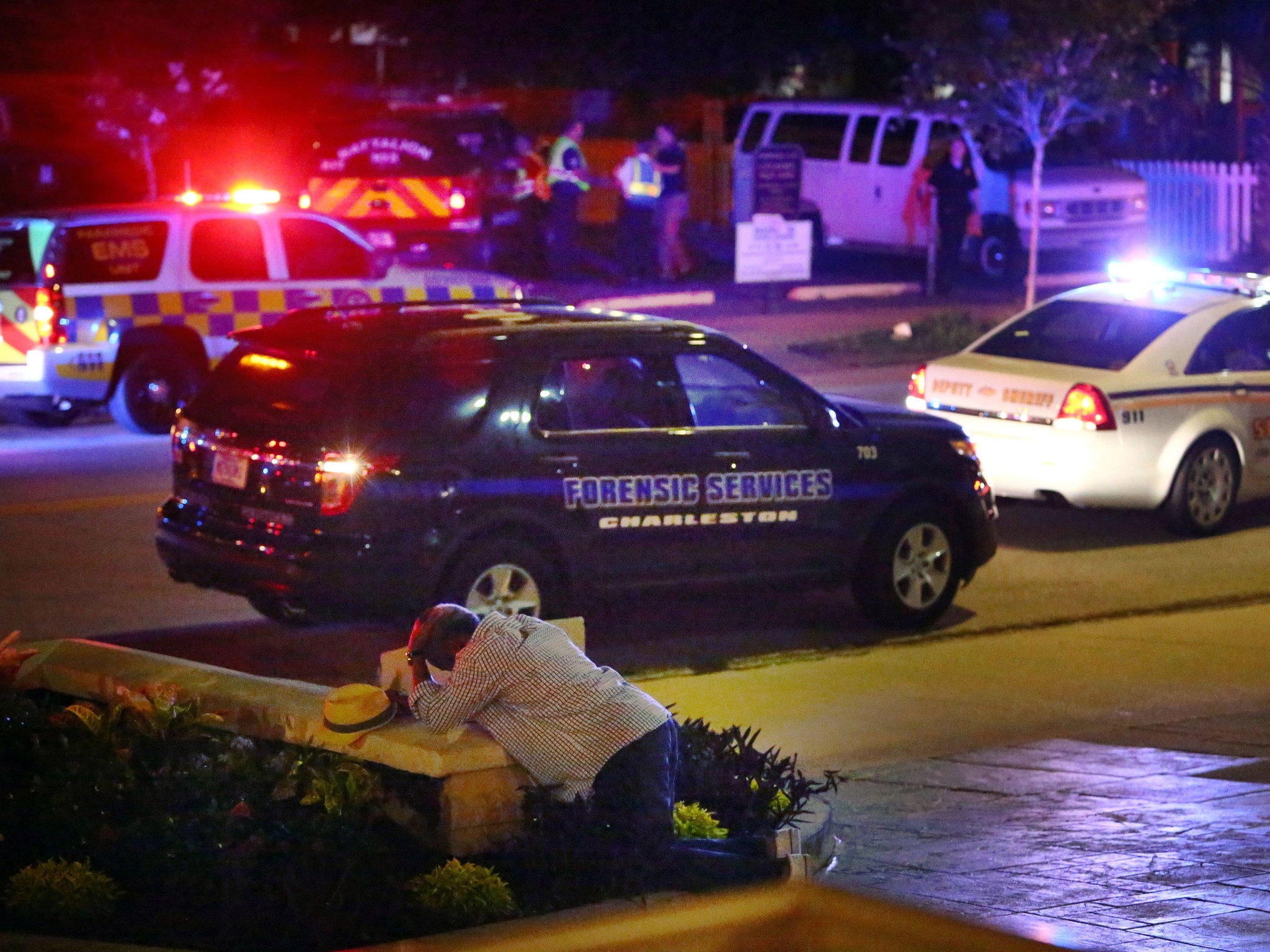 A man kneels across the street from where police gather following a shooting