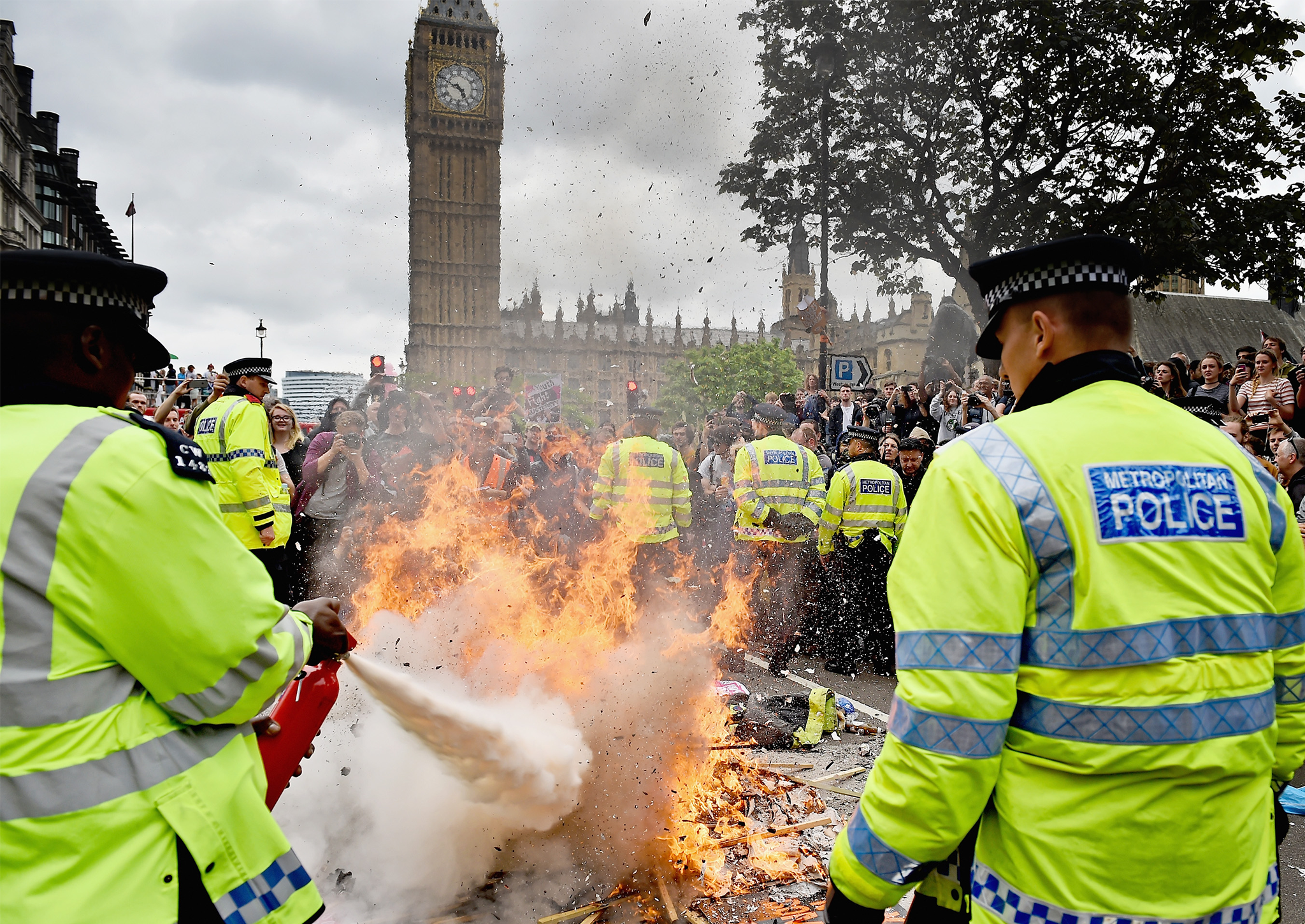 Police put out a fire started by protesters in central London during a demonstration against austerity and spending cuts on June 20, 2015 in London