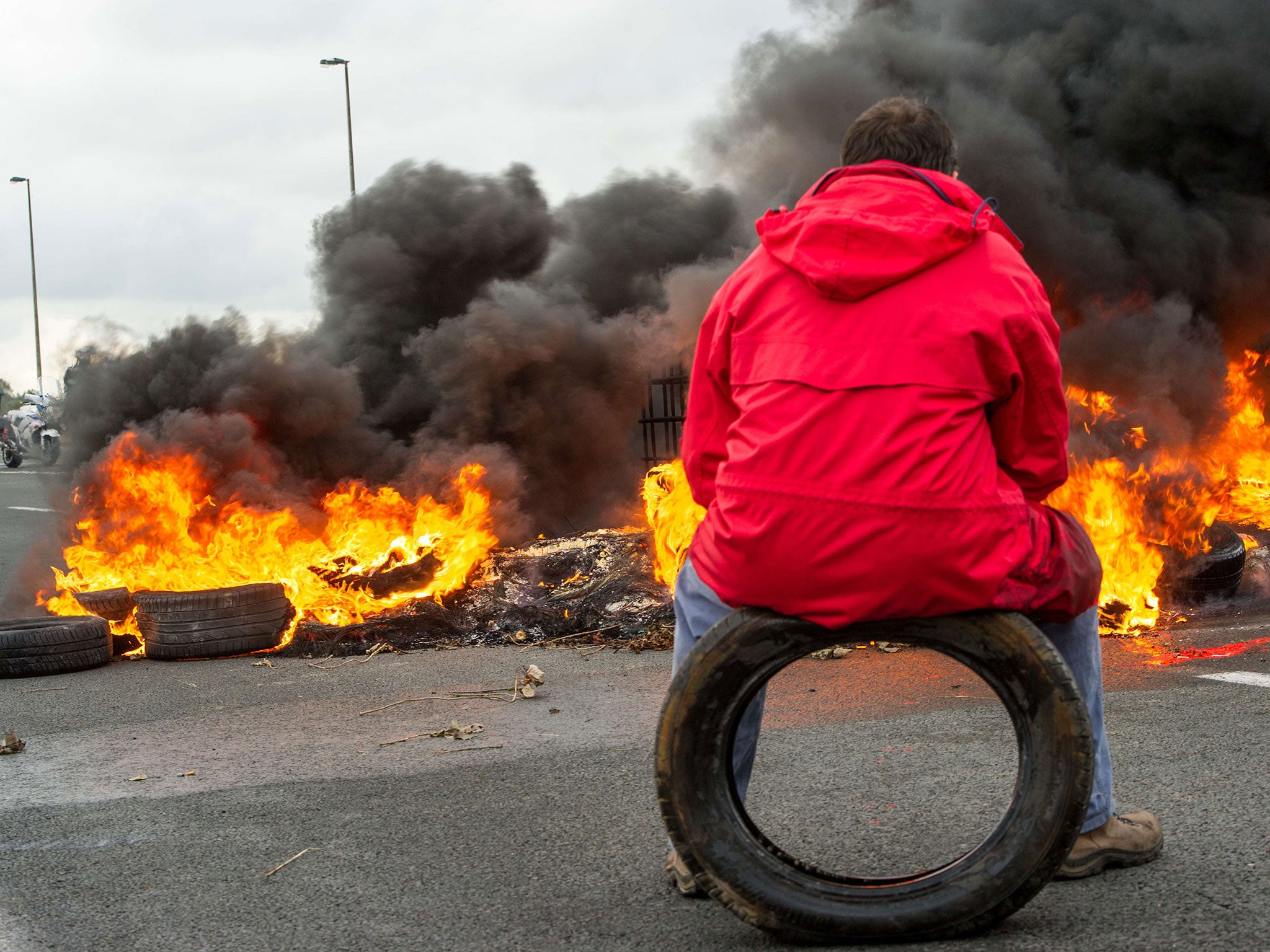 A striking employee sits on a tyre in front of tyres set on fire as he takes part in a blockade