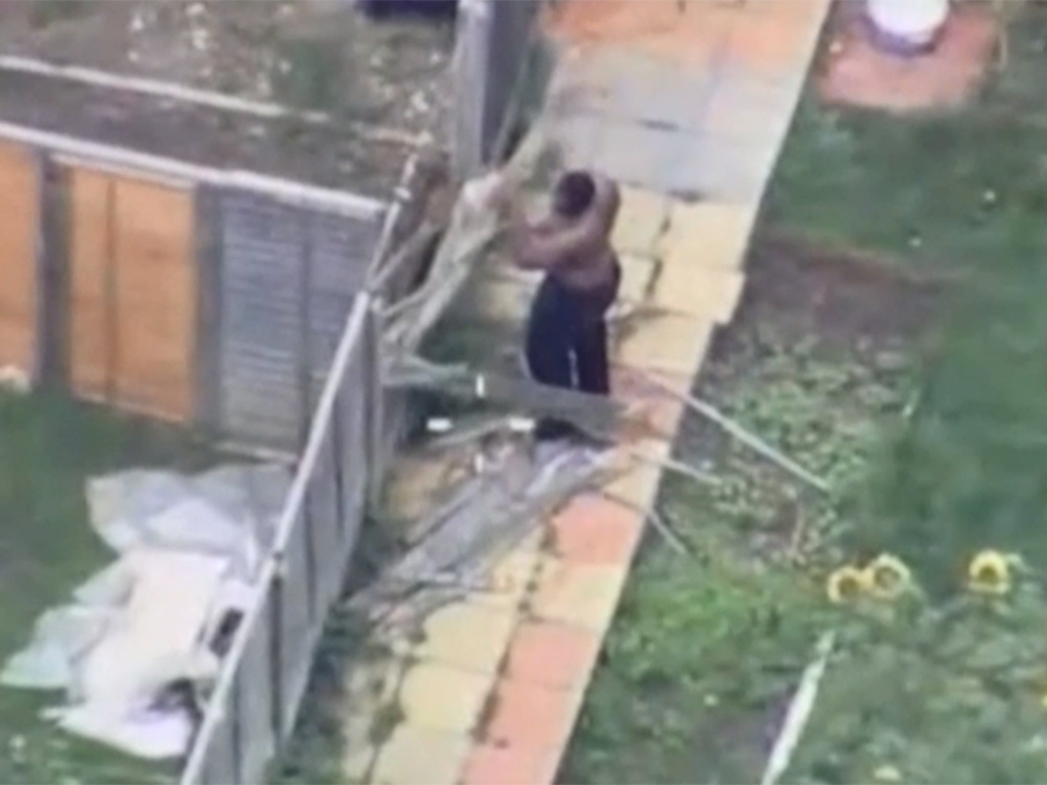 He then takes down a fence just yards from young children. A police officer climbs a nearby roof to tell them to get inside.