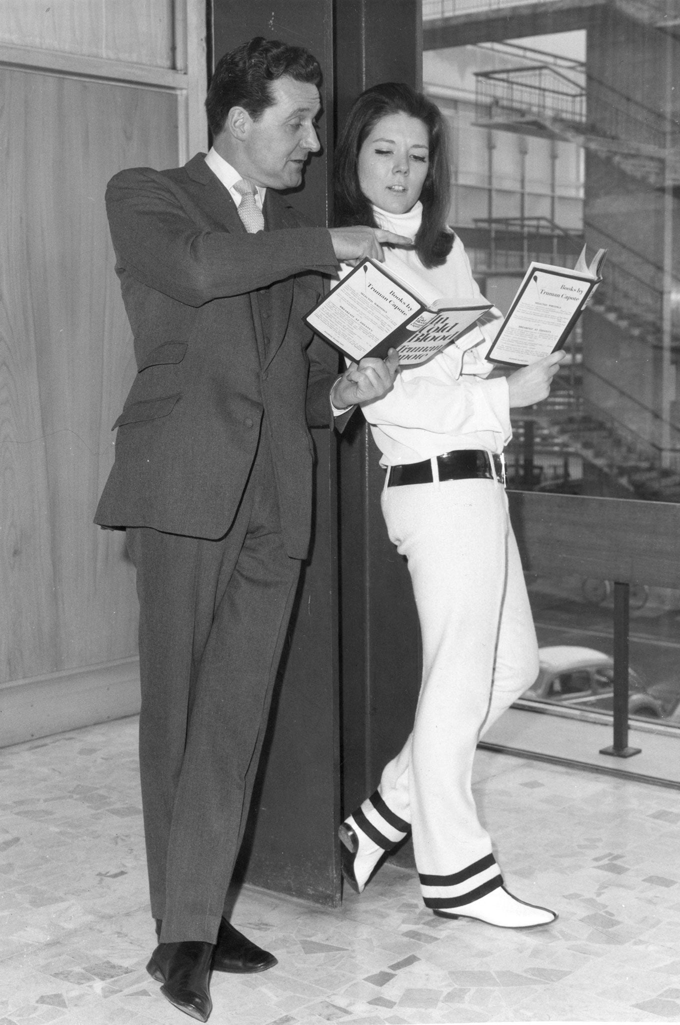 Patrick Macnee and Diana Rigg, reading Truman Capote's 'In Cold Blood' as they wait at London Airport to travel across the United States to promote their television series, 'The Avengers'