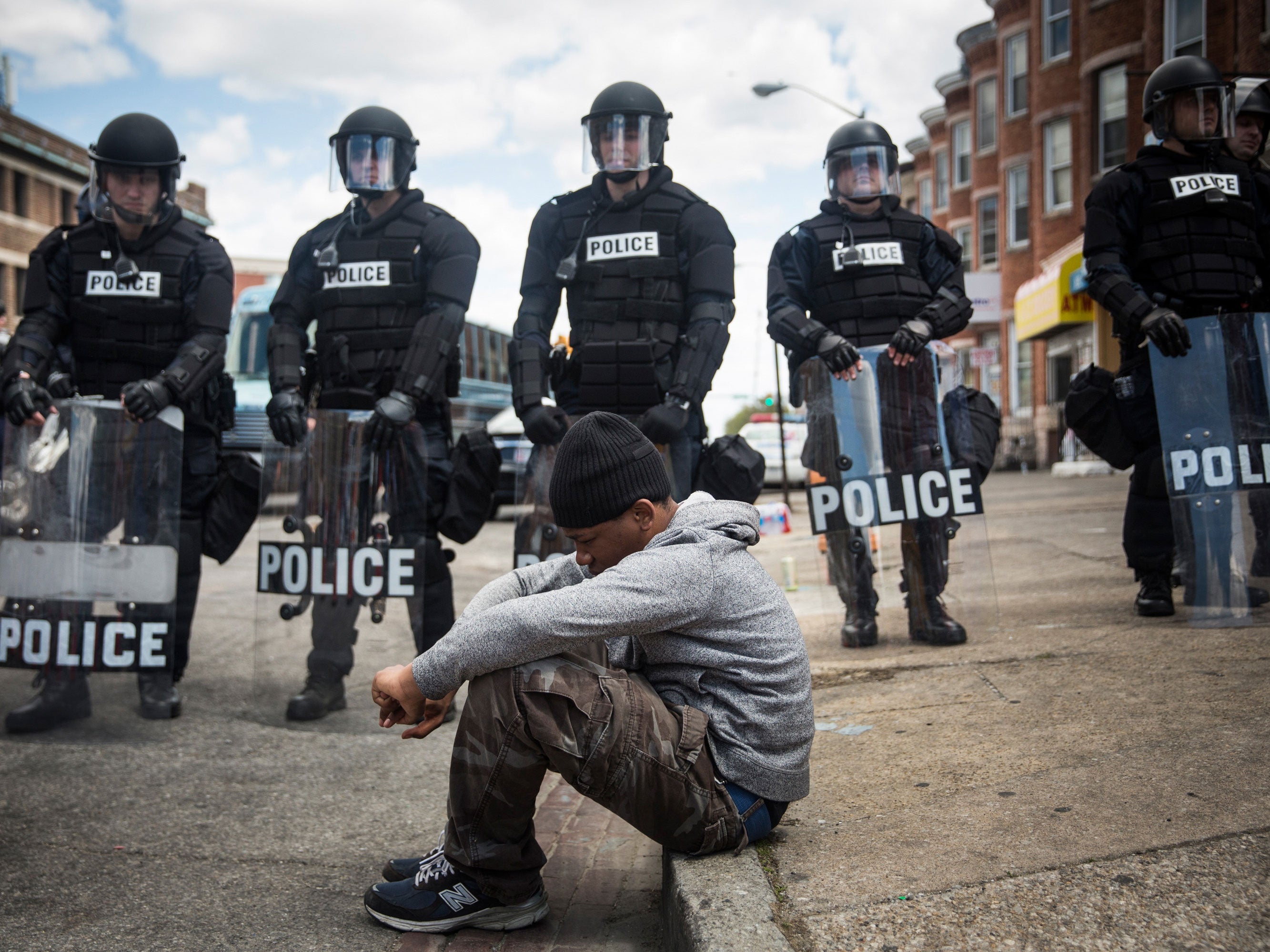 Daquan Green, age 17, sits on the curb while riot police stand guard