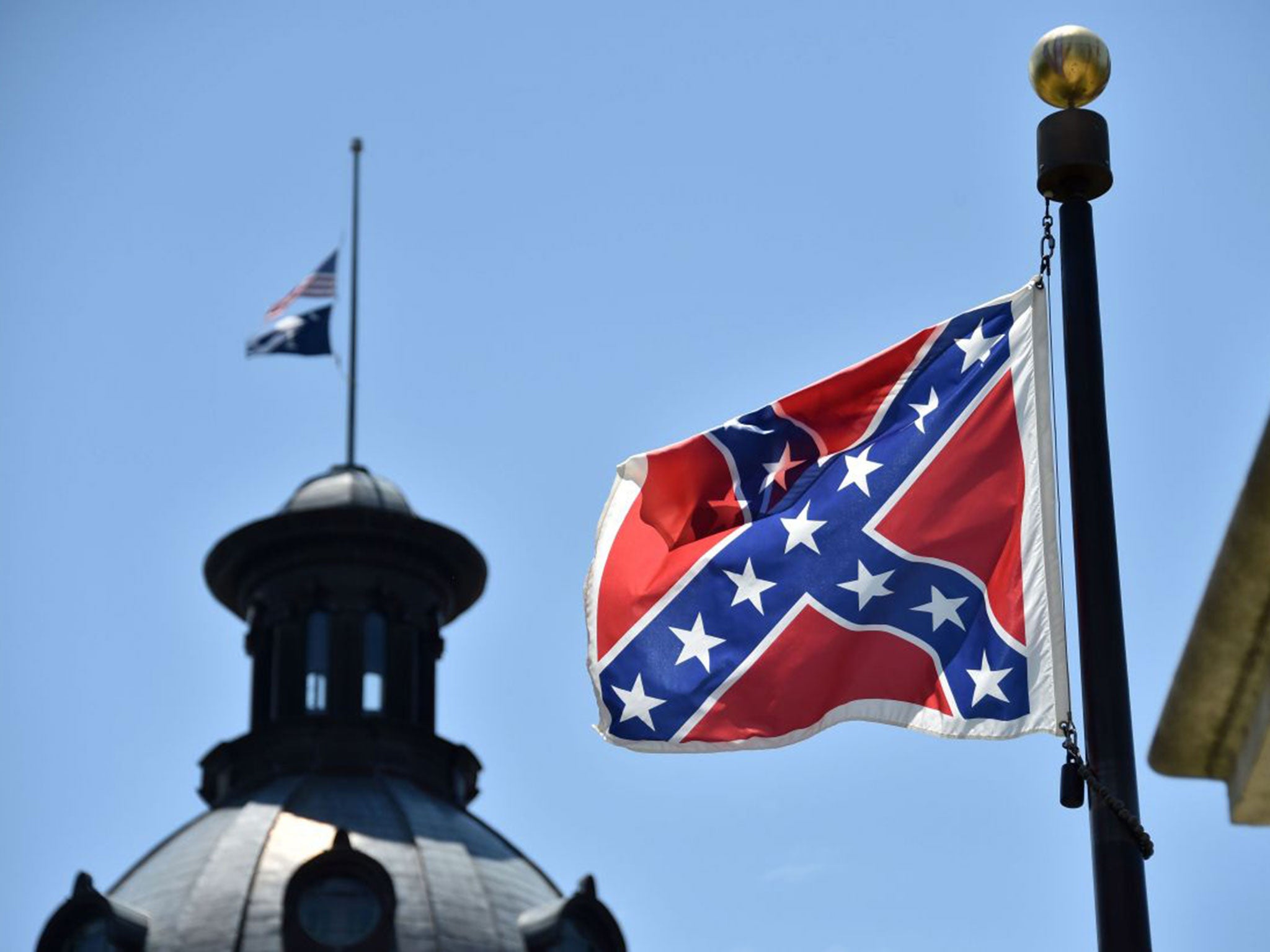 The South Carolina and US flags are seen flying at half-staff behind the Confederate flag