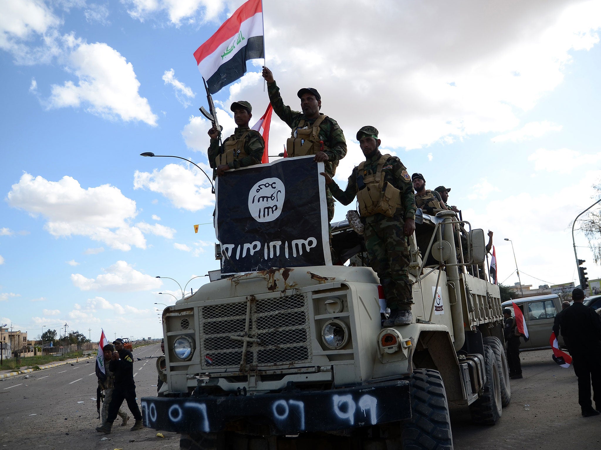 Shiite fighters from the Popular Mobilisation units celebrate on a truck with a national flag and a board they seized from the Islamic State