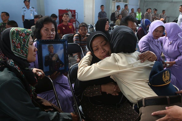 Relatives of military personnel killed grieve together during a send-off ceremony at the military airbase in Medan this morning