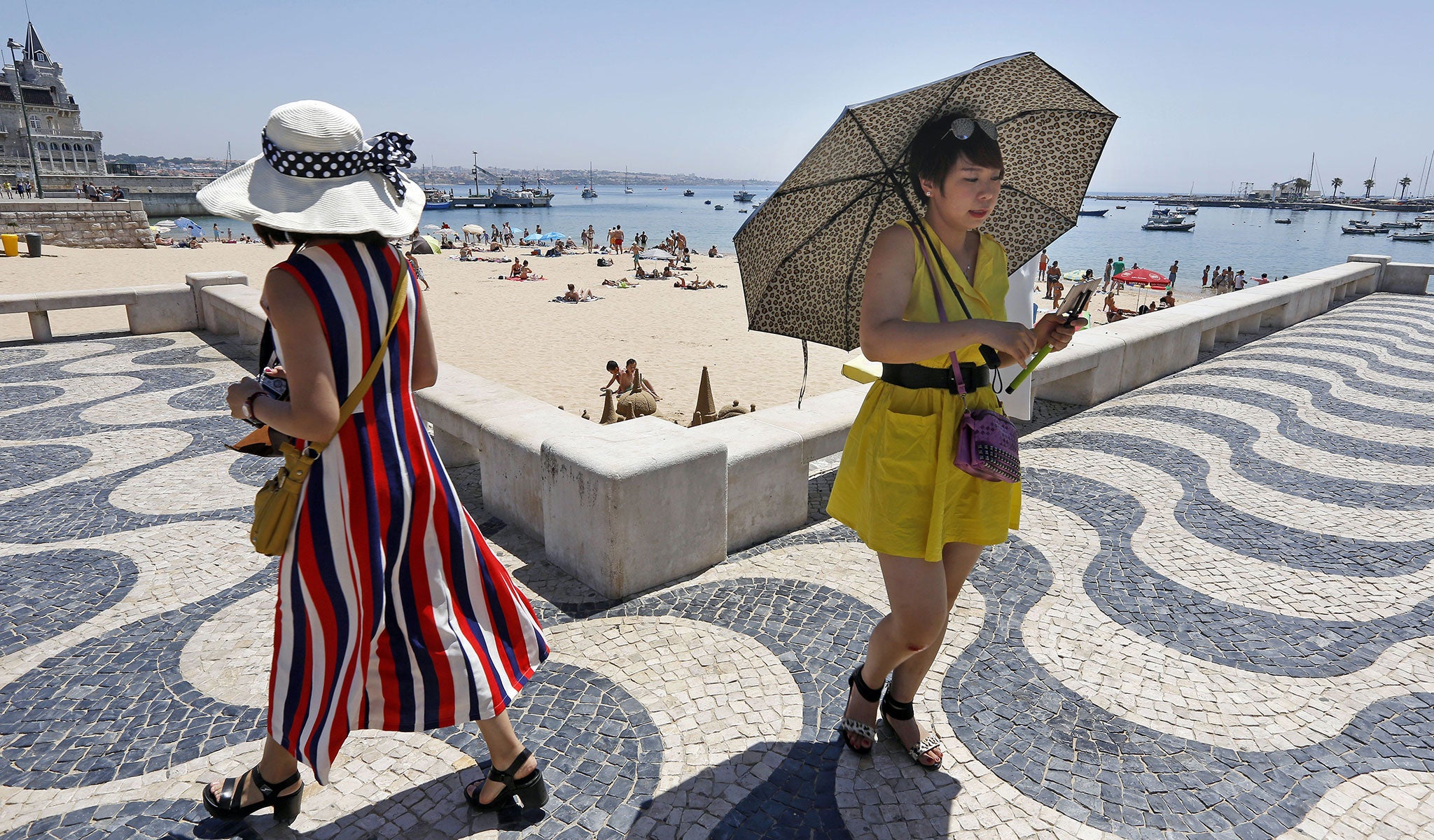 A tourist uses an umbrella to protect from the sun as she goes for a walk by Cascais' beach on the outskirts of Lisbon