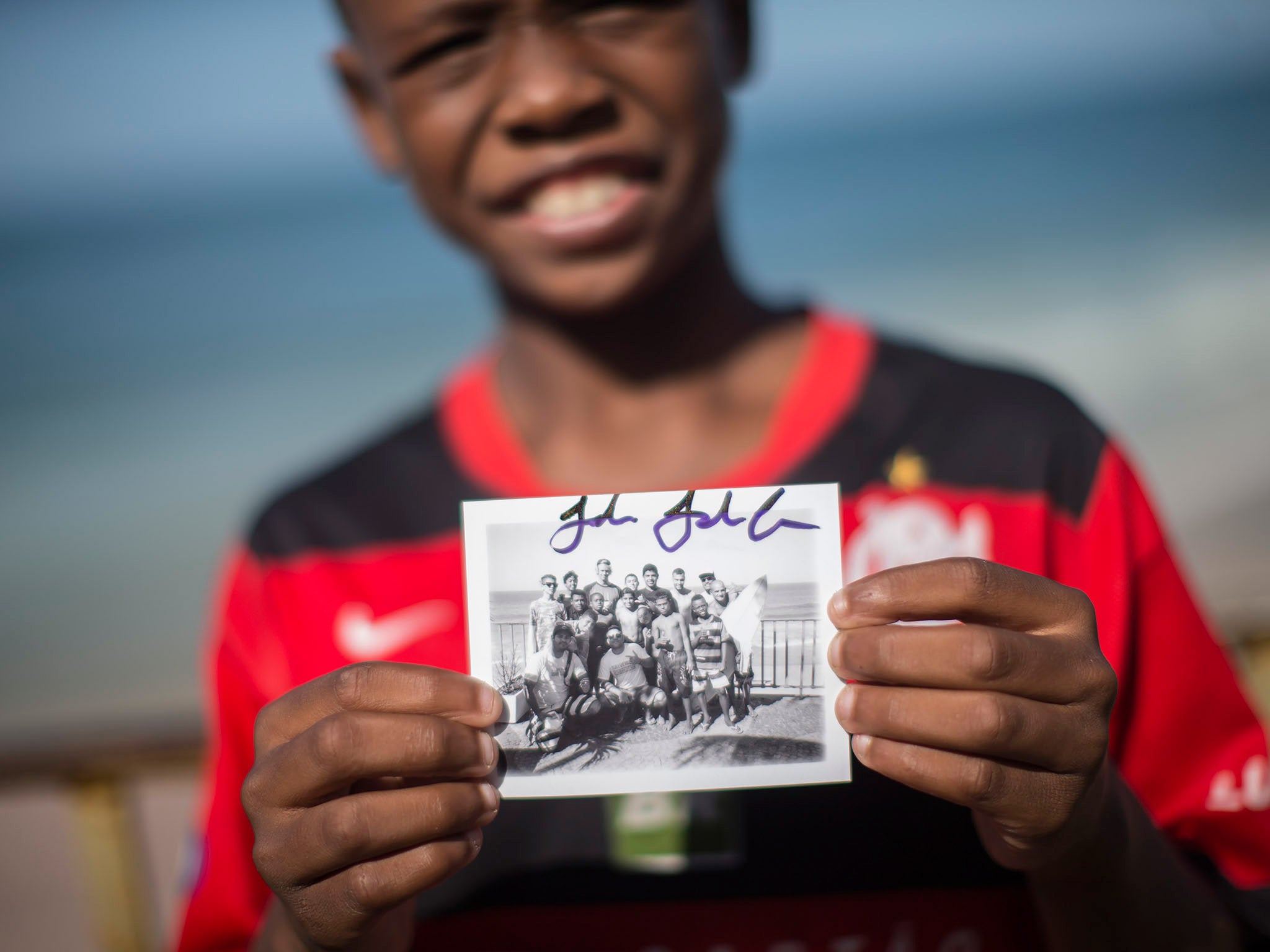 In this May 21, 2015 photo, Christian da Conceicao, 11, shows a signed polaroid photo of him and friends with U.S. surfer John John Florence at Sao Conrado beach in Rio de Janeiro, Brazil. Everyday barefoot boys hustle down the inclined alleyways of the Rio de Janeiro slums they call home, surf boards under their arms. (AP Photo/Felipe Dana)