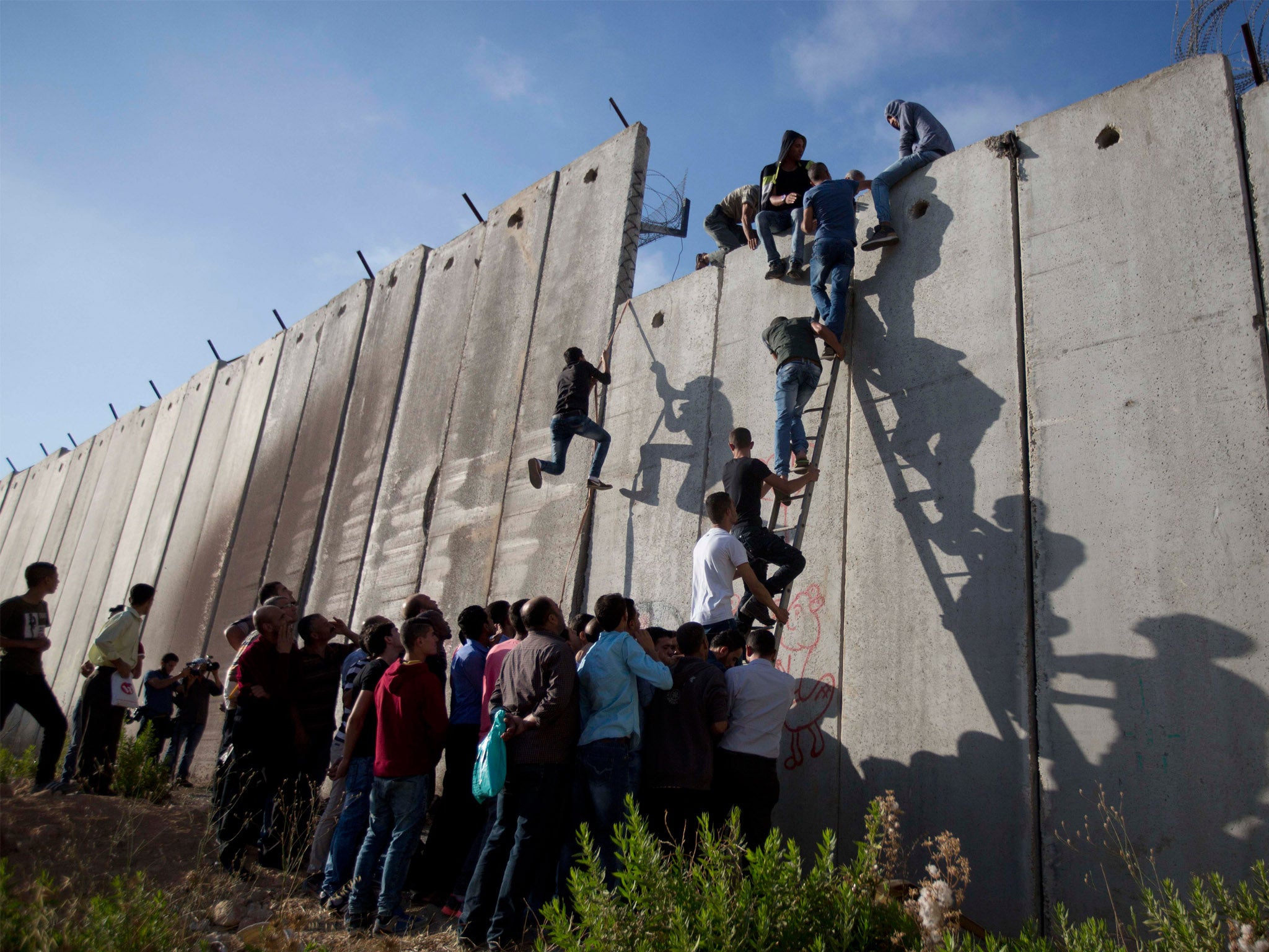 Palestinians use a ladder to climb over the separation barrier with Israel on their way to pray at the Al-Aqsa Mosque on the third Friday of the Muslim holy month of Ramadan, in Al-Ram, north of Jerusalem, Friday, 26 June 2015