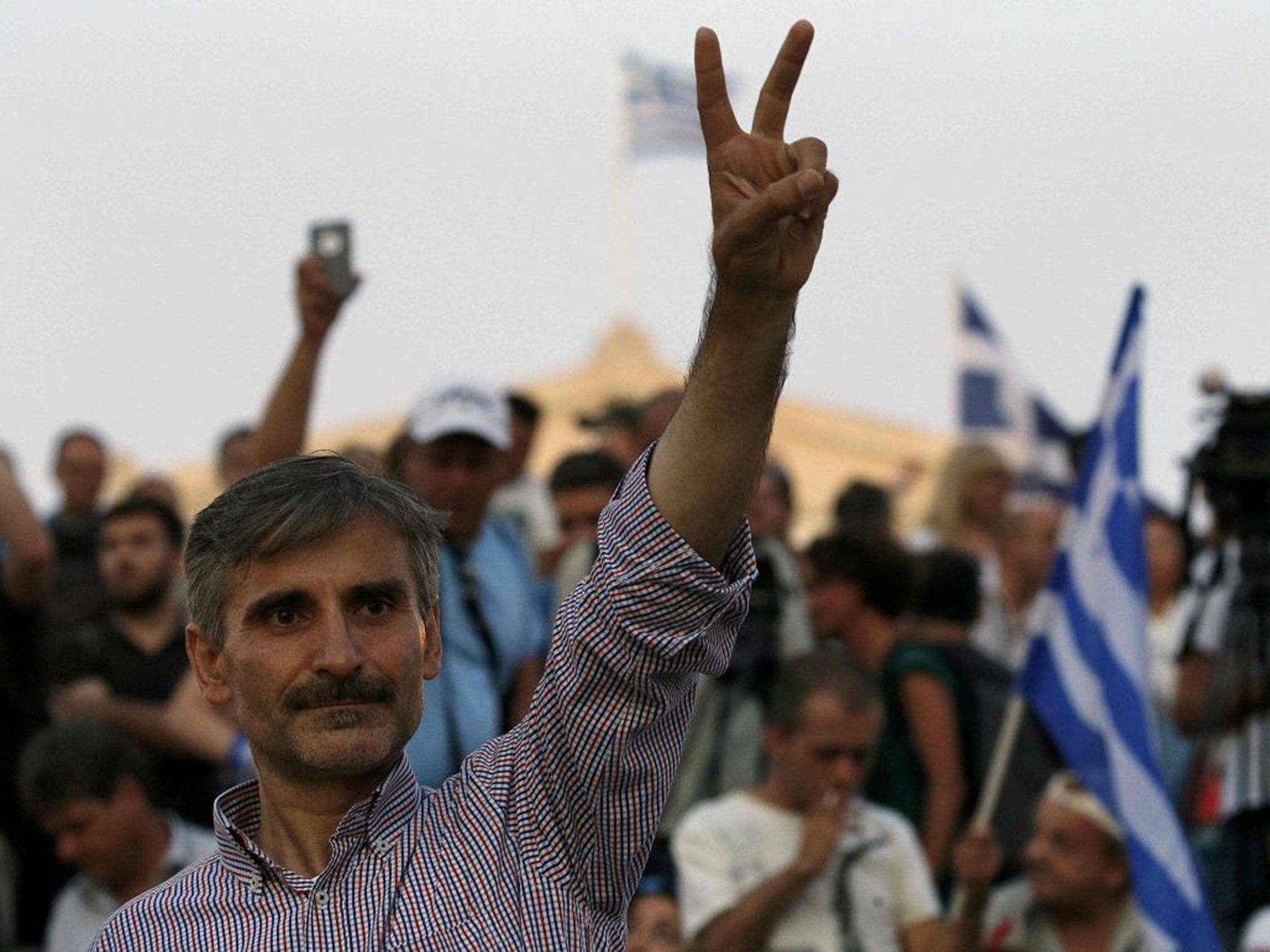 A "No" supporter flashes a victory sign before a Greek flag atop the parliament in Athens (AFP/YANNIS BEHRAKIS)