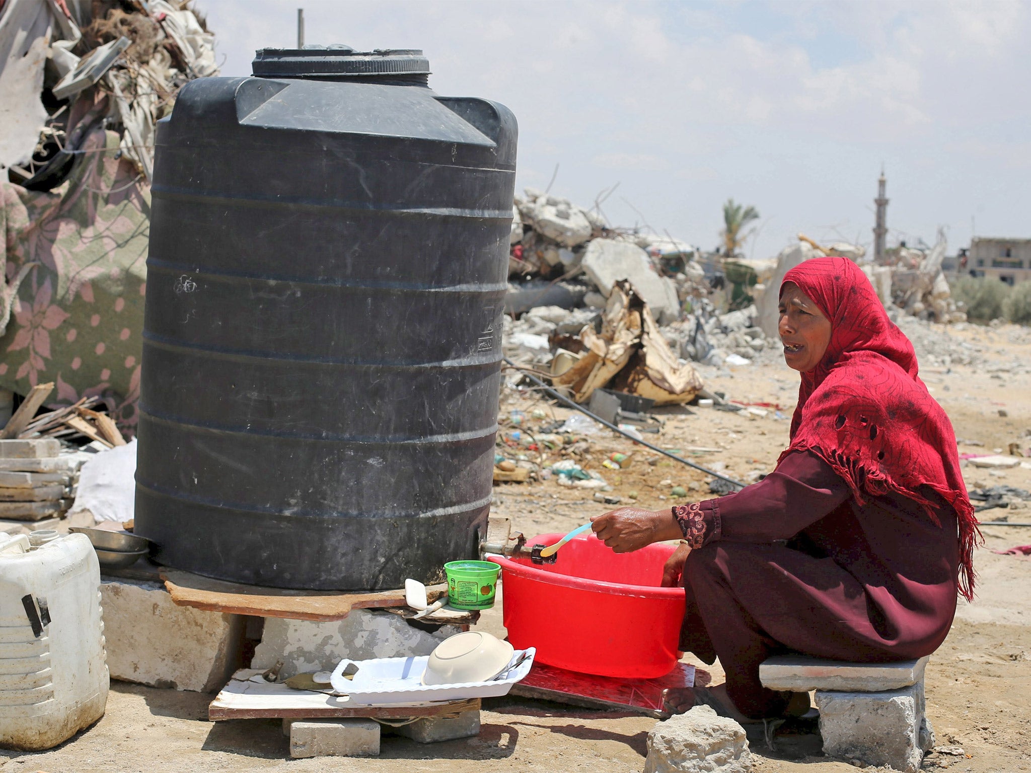 A Palestinian woman fills water from a tank near the remains of her house, in Khan Younis, Gaza