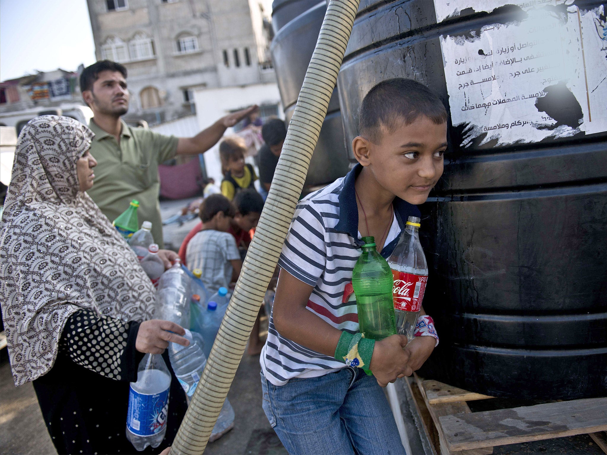 Palestinians, displaced by violence and living at a UN school in Gaza City, fill up their plastic jugs as a water supply truck makes its daily delivery (Getty)