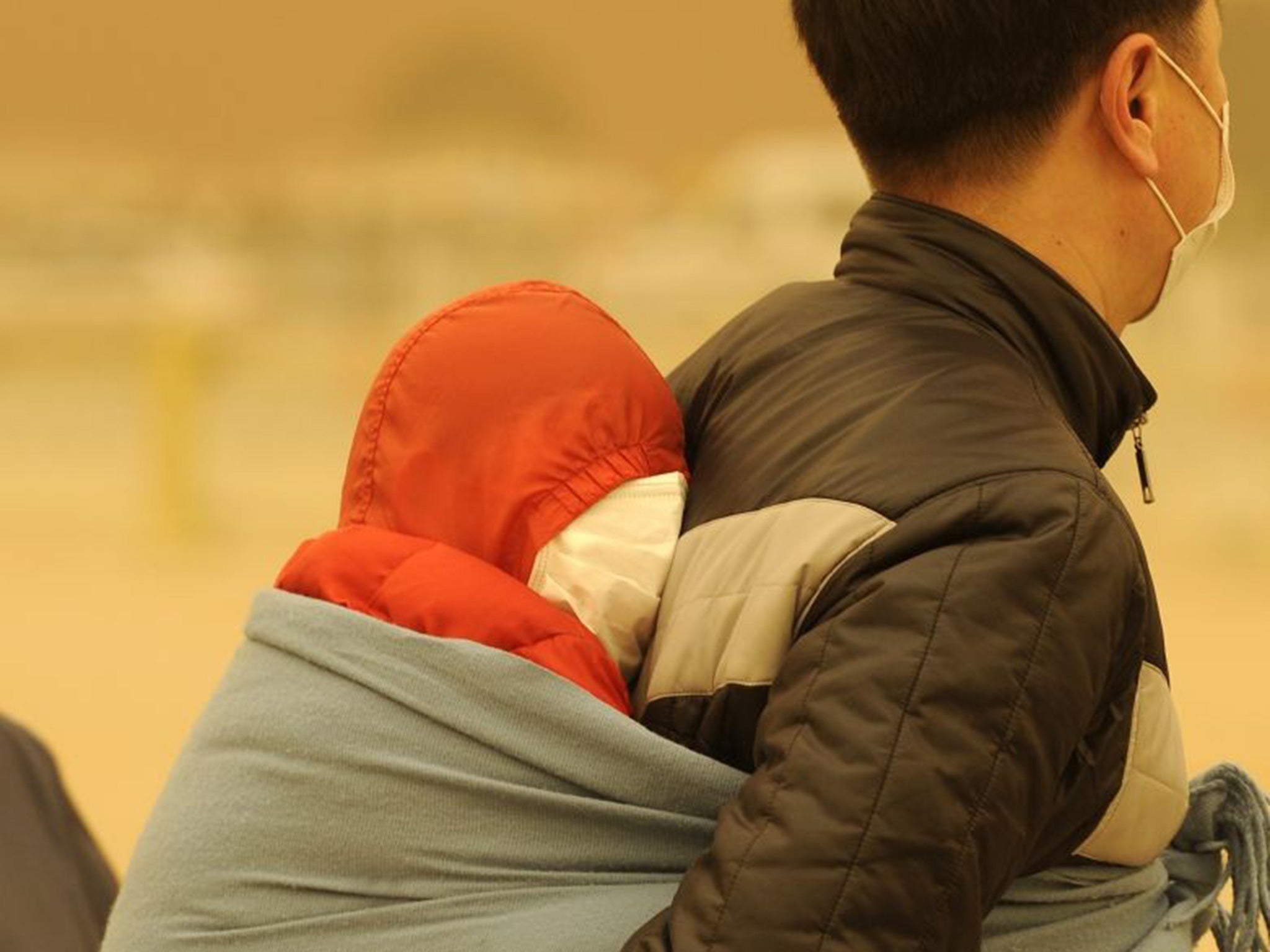 A man carries a baby wrapped up against a sandstorm in Beijing in 2010