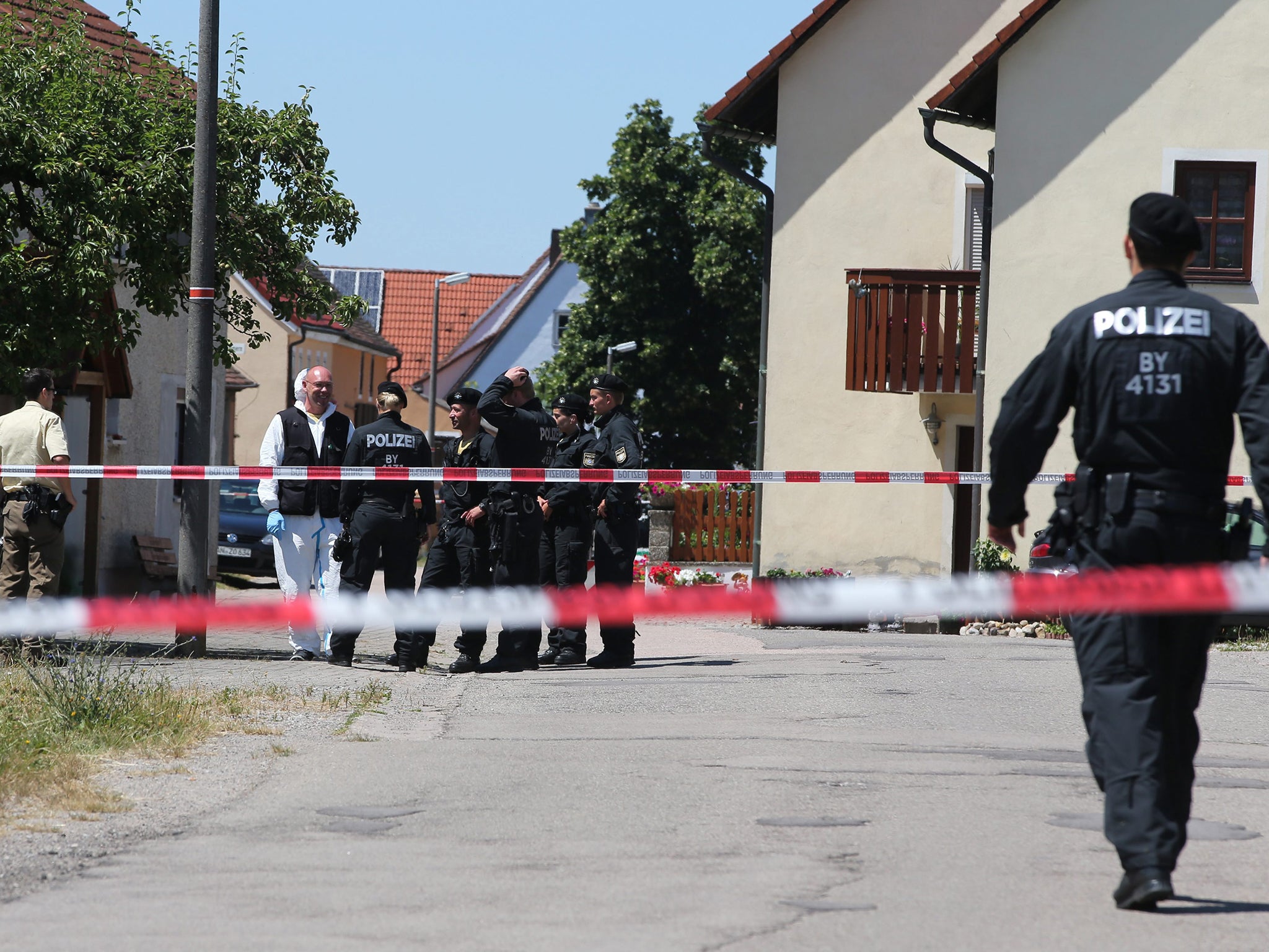 Crime scene investigators and police stand behind a police barrier band near a crime scene in Leutershausen, near Ansbach in Bavaria, Germany