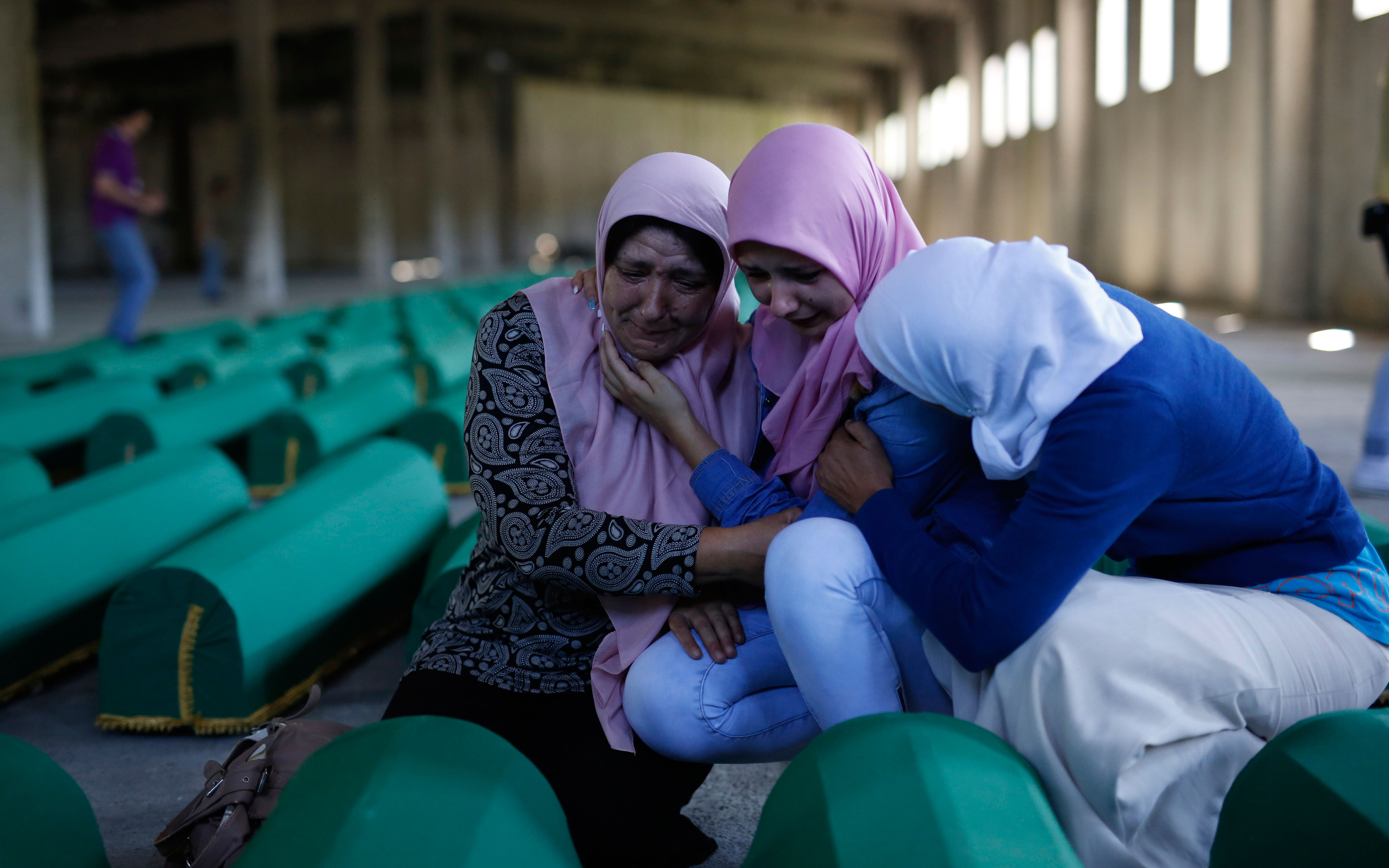 Women mourn over coffins set to be interred during Saturday's remembrance events