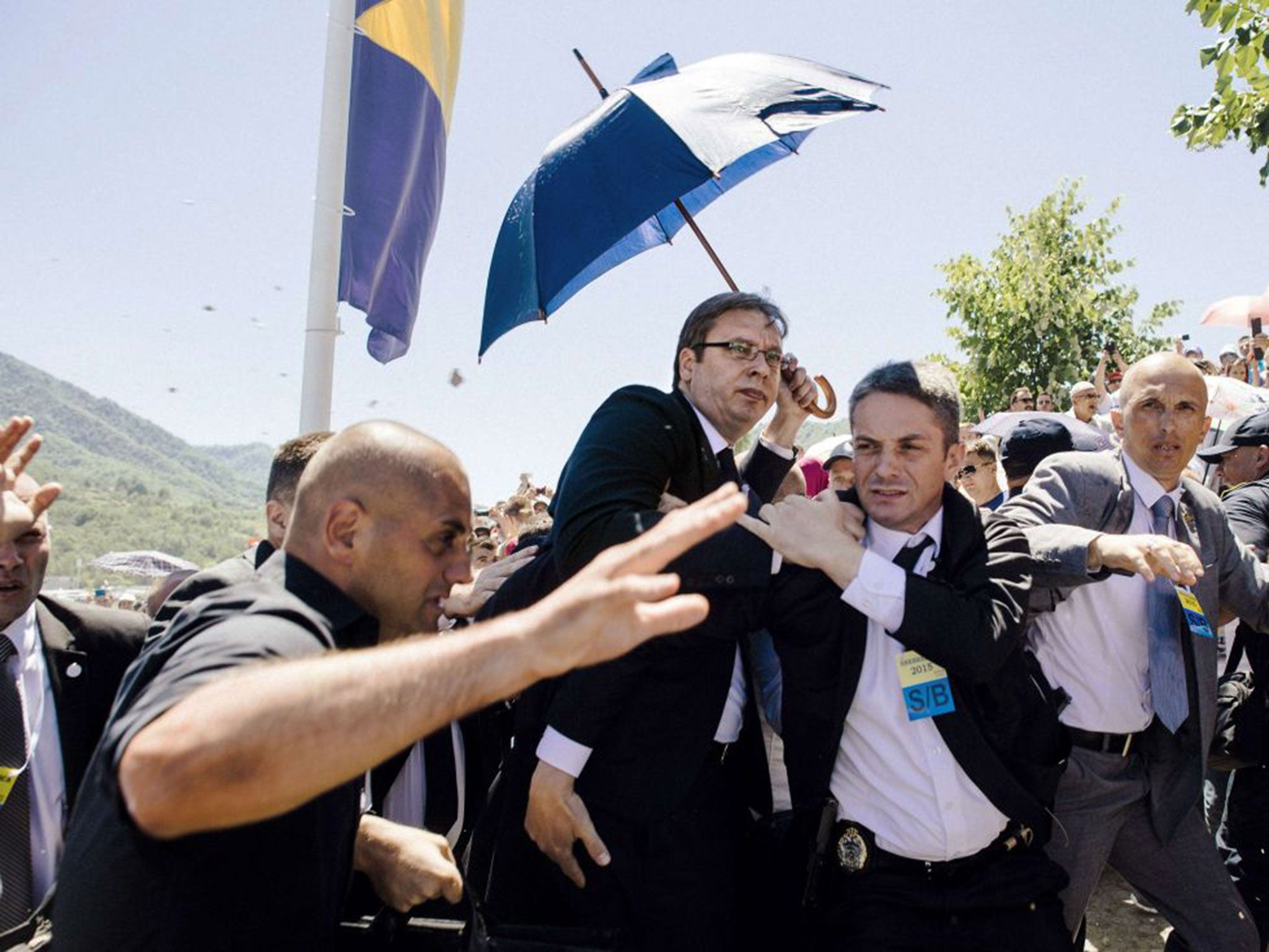 Bodyguards try to protect Serbian Prime Minister Aleksandar Vucic (C) from stones hurled at him by an angry crowd at the Potocari Memorial Center