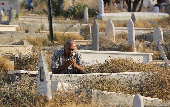 A man reads D'uaa by the grave of a family member this morning at a cemetery in Gaza City's eastern suburb of Al-Shejaiya (via MAHMUD HAMS/AFP/Getty Images)