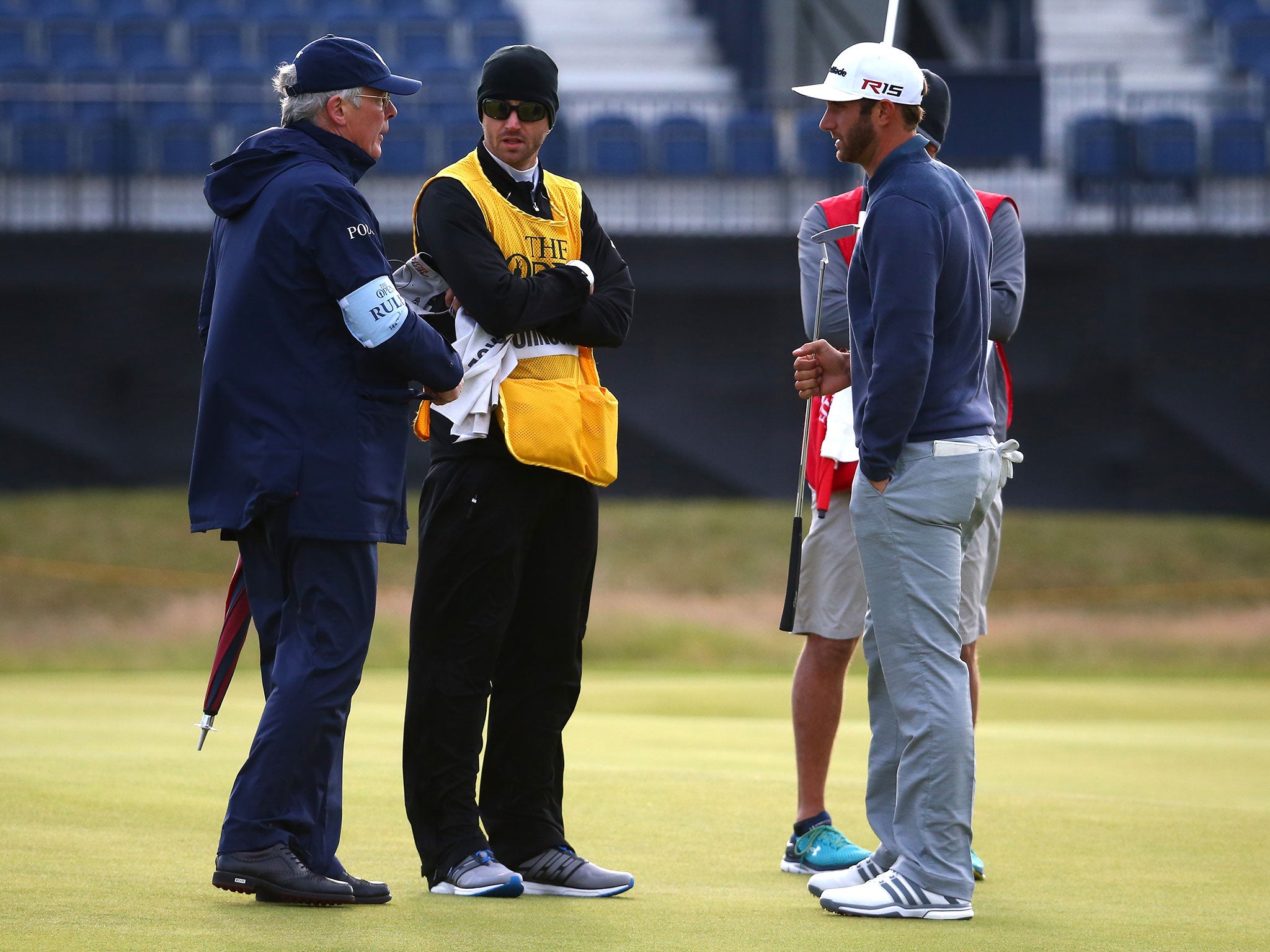 Dustin Johnson speaks with officials after his ball is blown off the green