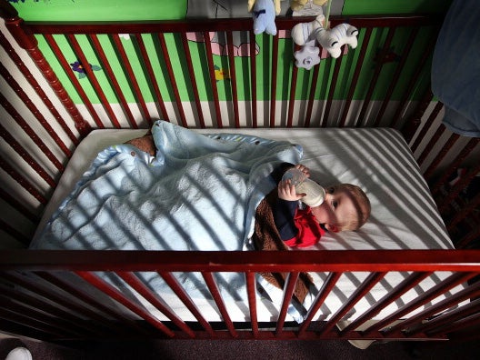 An 8-month-old drinks a bottle in a cot