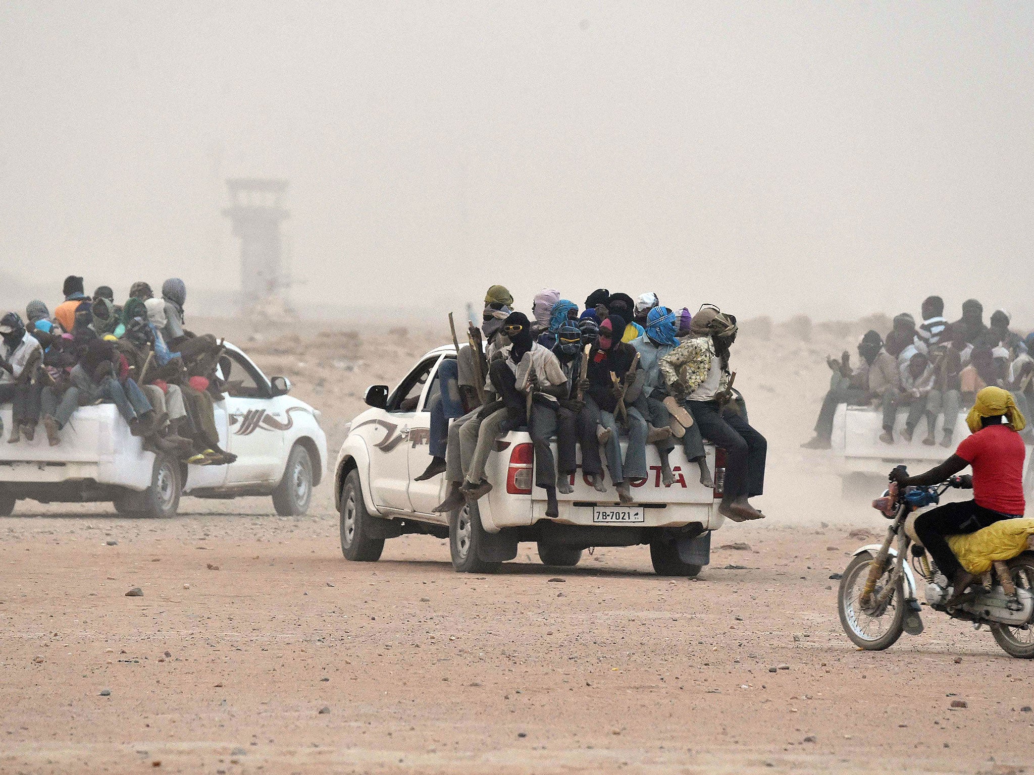 Migrants sit on the open cargo of pick-up trucks, holding wooden sticks tied to the vehicle to avoid falling from it, as they leave the outskirts of Agadez for Libya