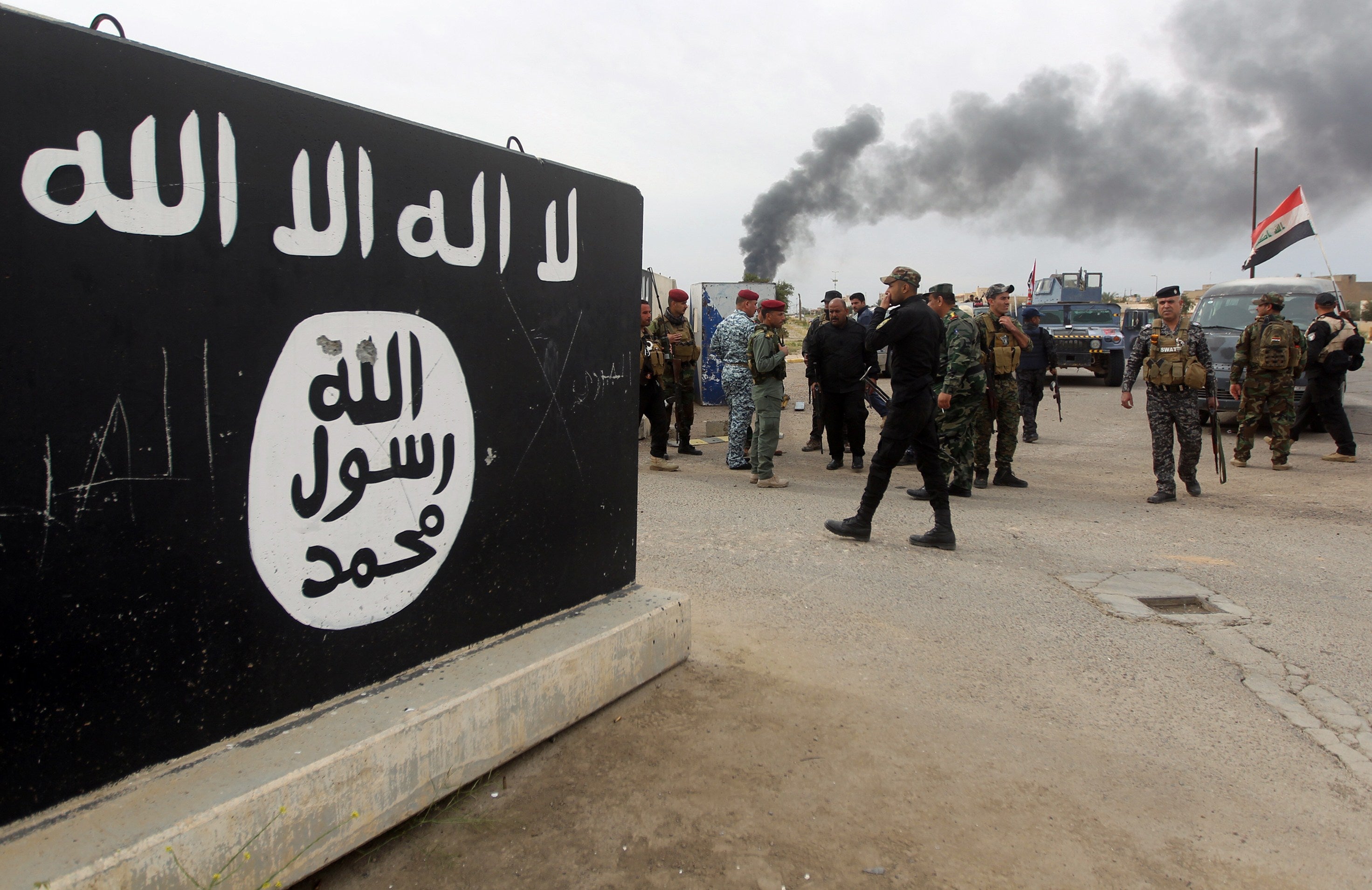 Iraqi security forces and Shiite fighters from the Popular Mobilisation units gather next to a mural depicting the emblem of Isis