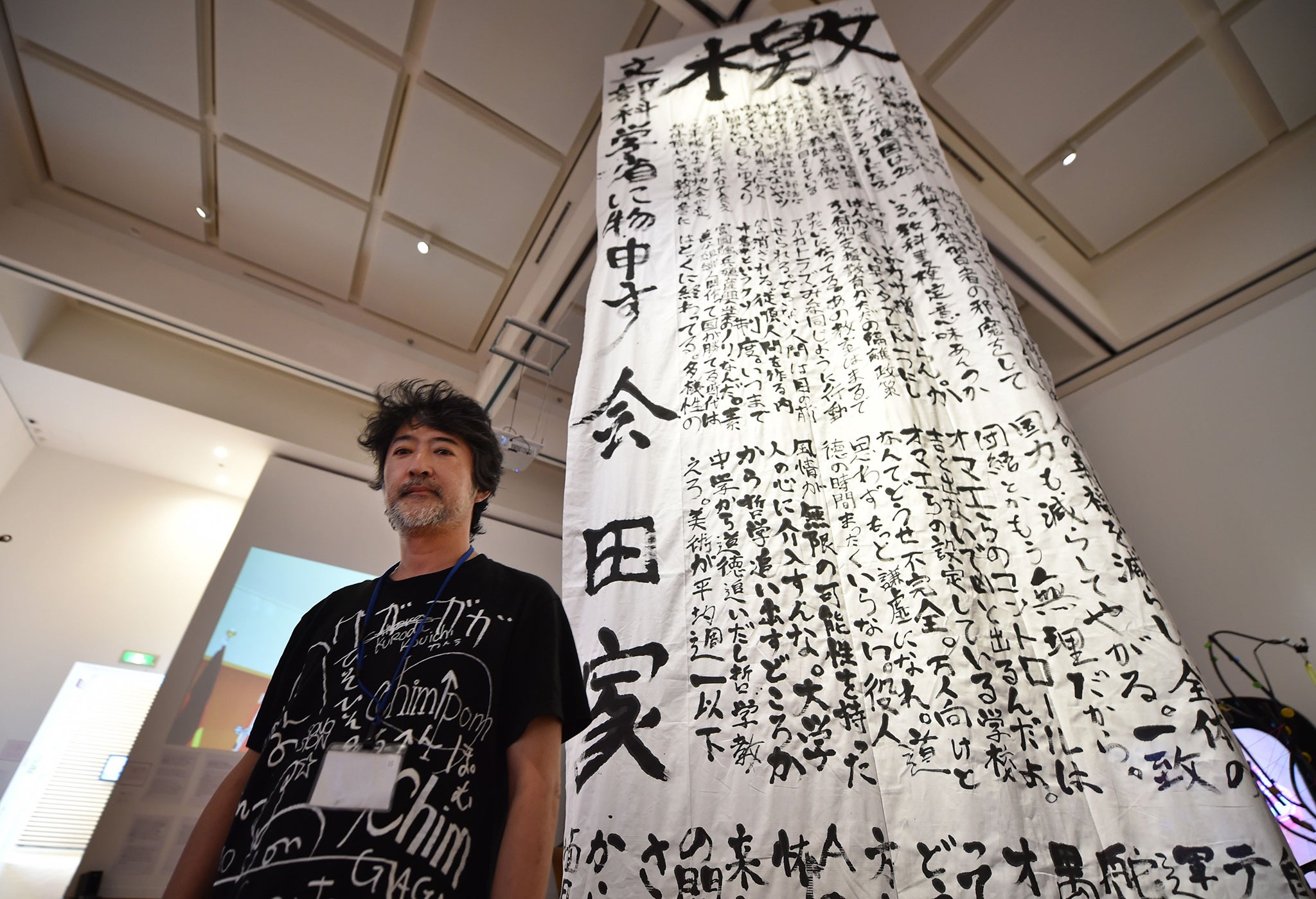 One of Japan's best-known contemporary artists Makoto Aida stands next to his work, a large calligraphy hanging from a ceiling that openly criticises the education ministry, at an art exhibition for children at the Museum of Contemporary Art Tokyo