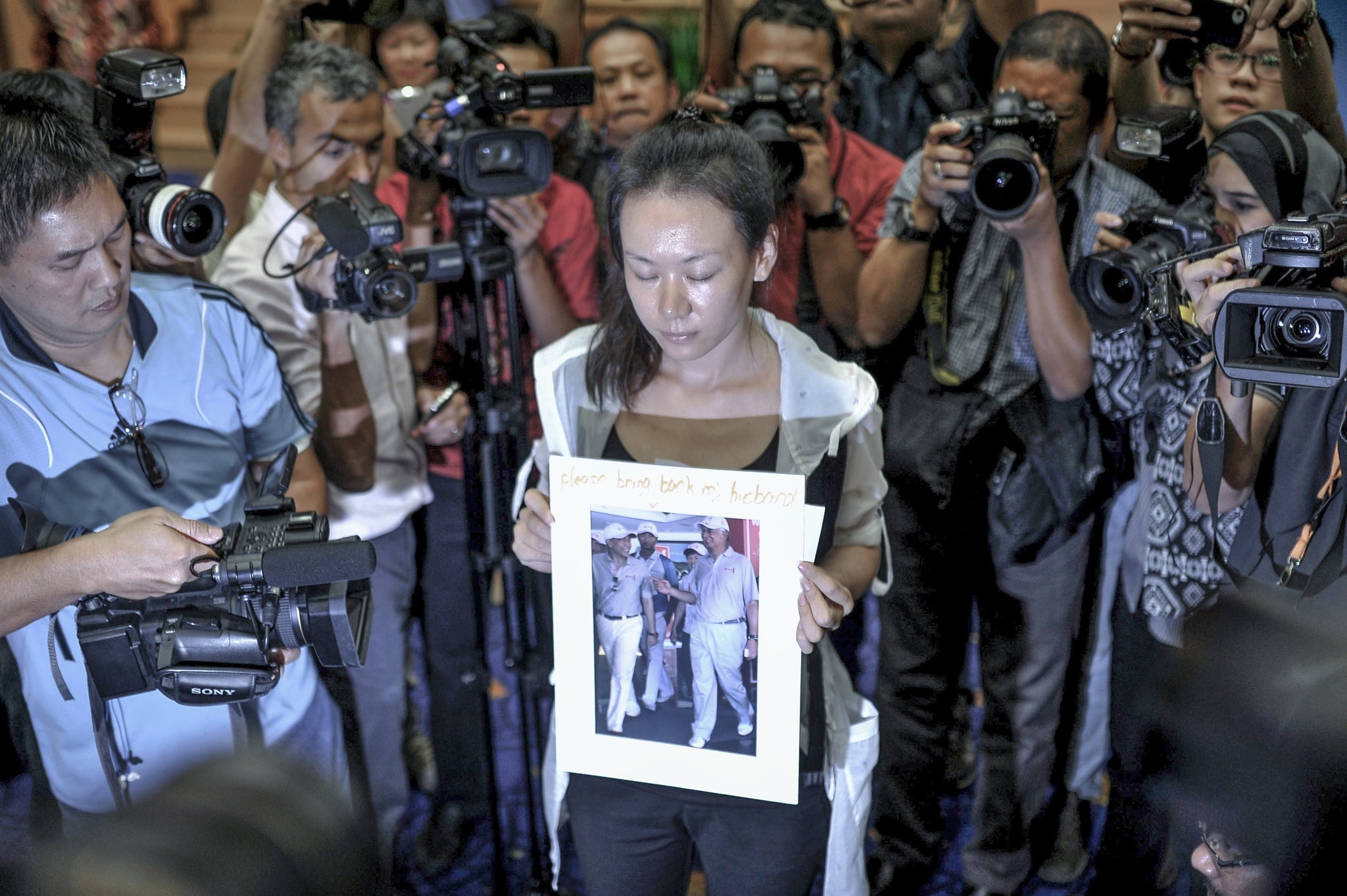 The wife of an MH370 victim holds a sign that reads 'Please bring back my husband' after the Malaysian Prime Minister cancels a press conference on the plane's disappearance