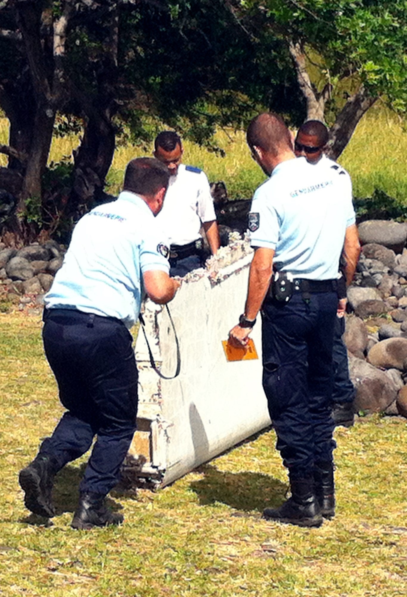 Policemen and gendarmes stand next to a piece of debris from an unidentified aircraft found in the coastal area of Saint-Andre de la Reunion, in the east of the French Indian Ocean island of La Reunion