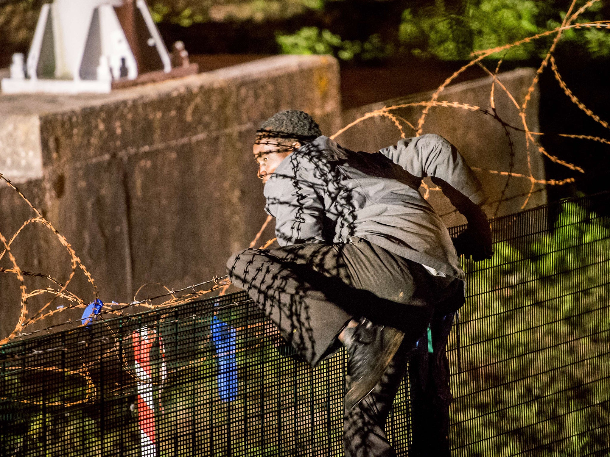 A migrant climbs a security fence of a Eurotunnel terminal in Coquelles near Calais