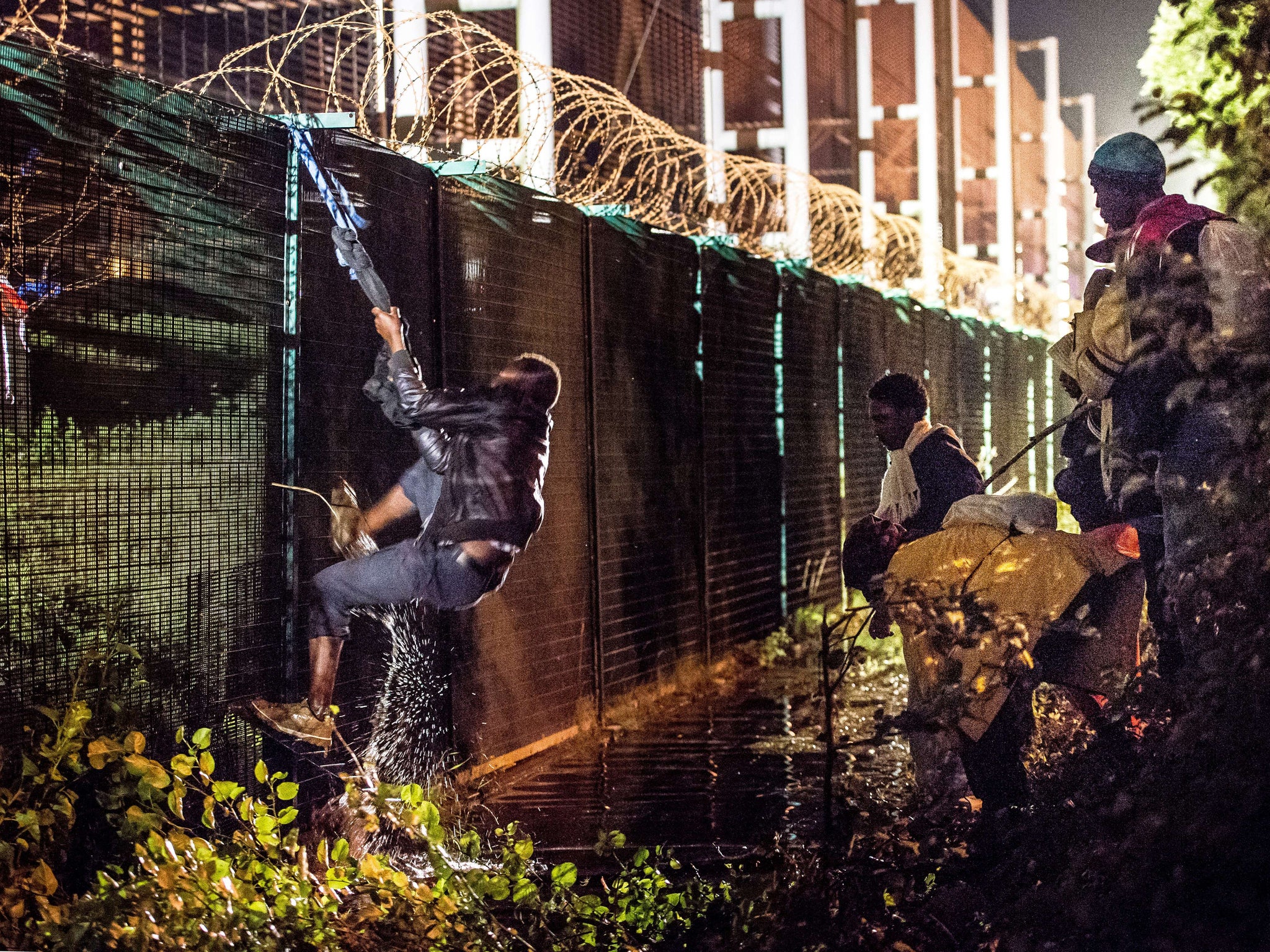 A migrant climbs a security fence of a Eurotunnel terminal in Coquelles near Calais