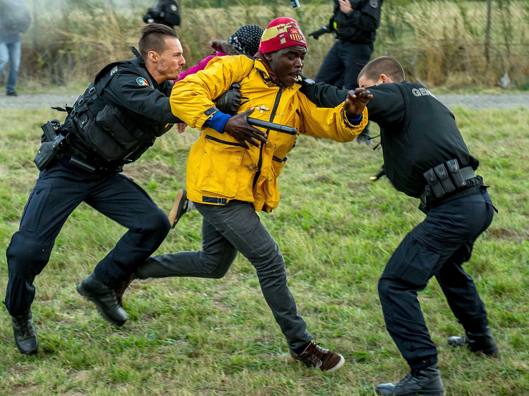 French gendarmes try to stop migrants on the Eurotunnel site in Coquelles near Calais