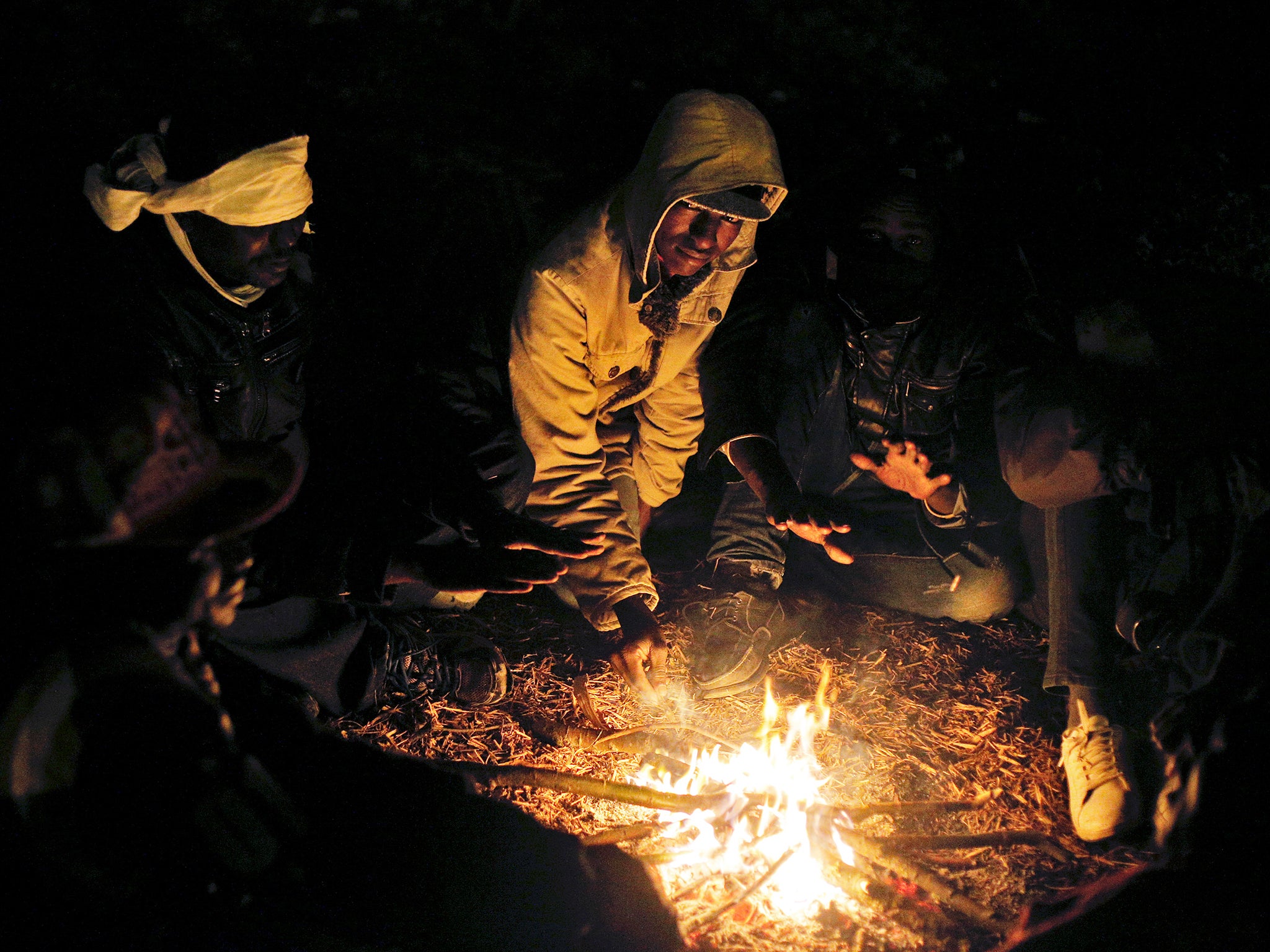 Migrants warm themselves with a fire as they attempt to access the Channel Tunnel, in Calais