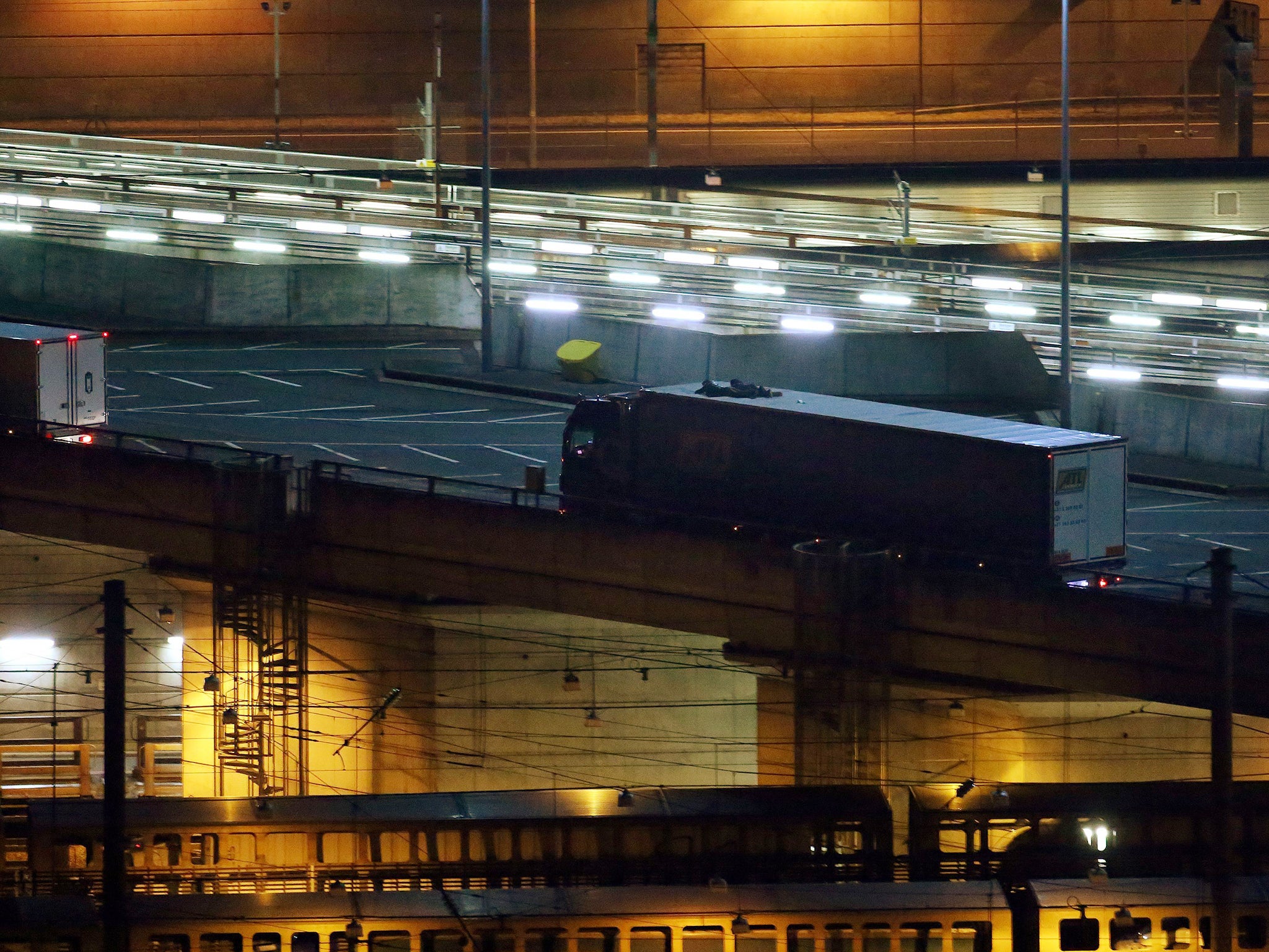 Two migrants cling to the top of a lorry as it leaves the Eurotunnel site in Folkestone, Kent