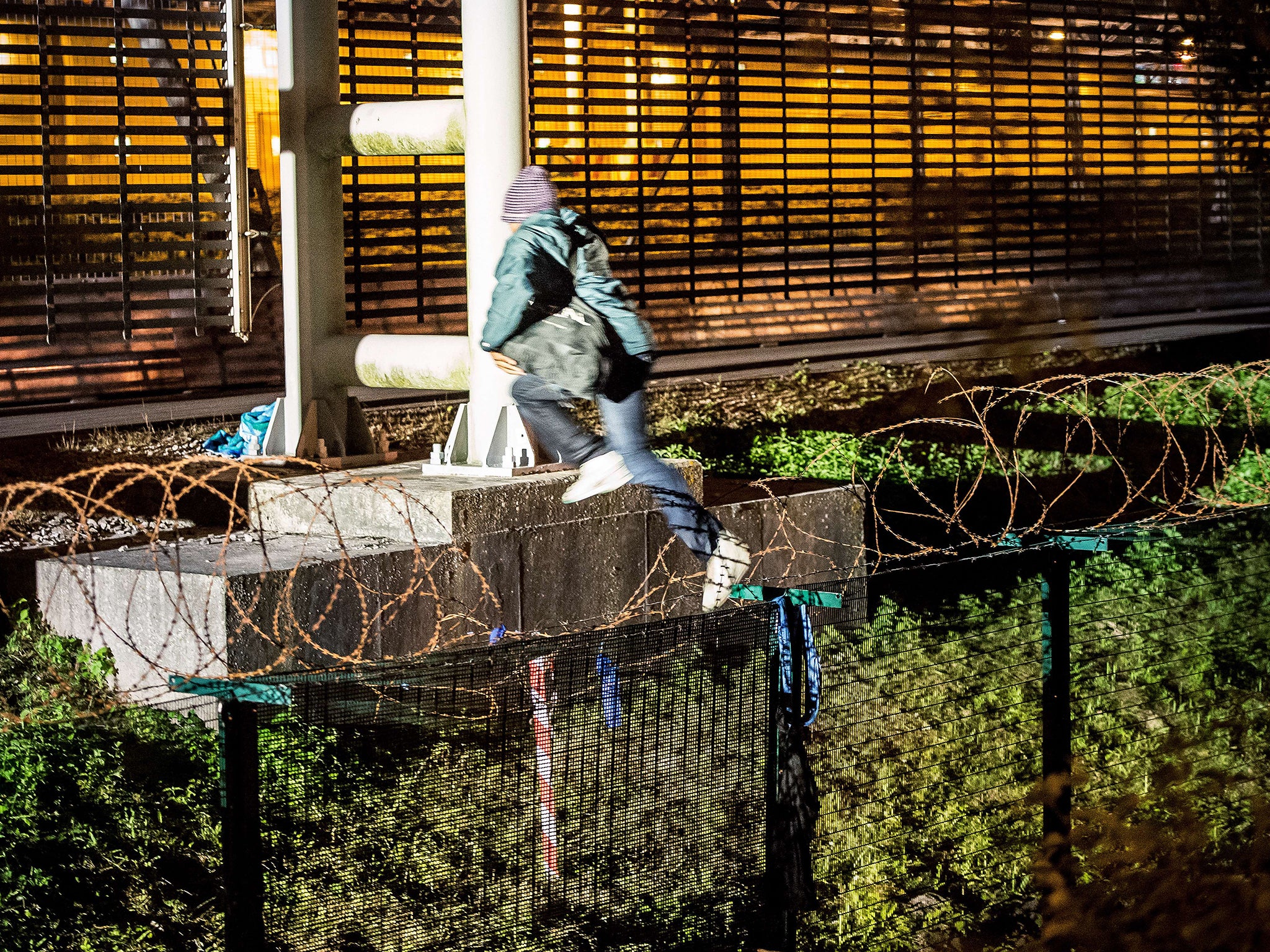 A migrant jumps after climbing a security fence of a Eurotunnel terminal in Coquelles near Calais