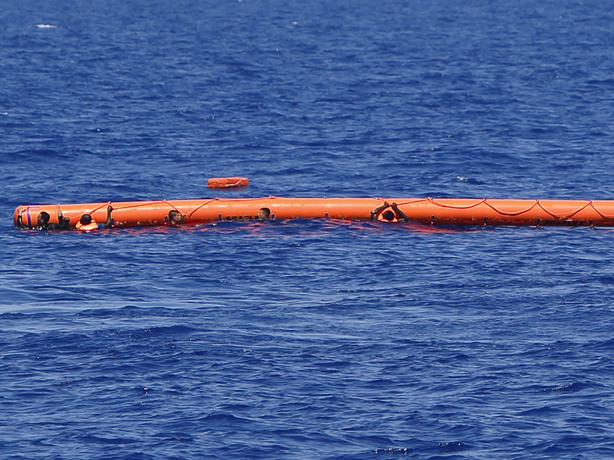 Migrants hang onto a flotation device during a rescue operation 10.5 miles (16 km) off the coast of Libya August 6, 2015