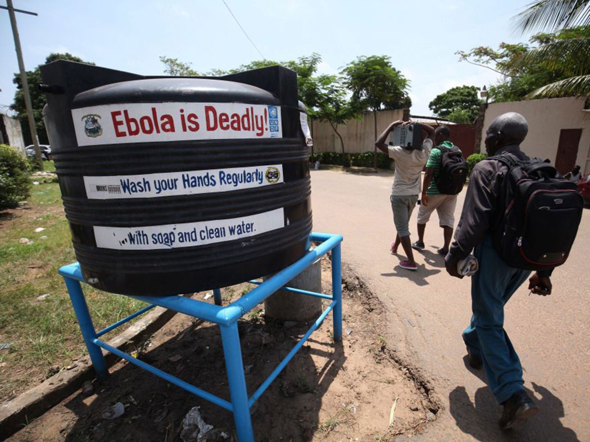 Liberians walk pass a public tank filled with chloronated water to curb the spread of the deadly ebola virus in Monrovia (EPA)