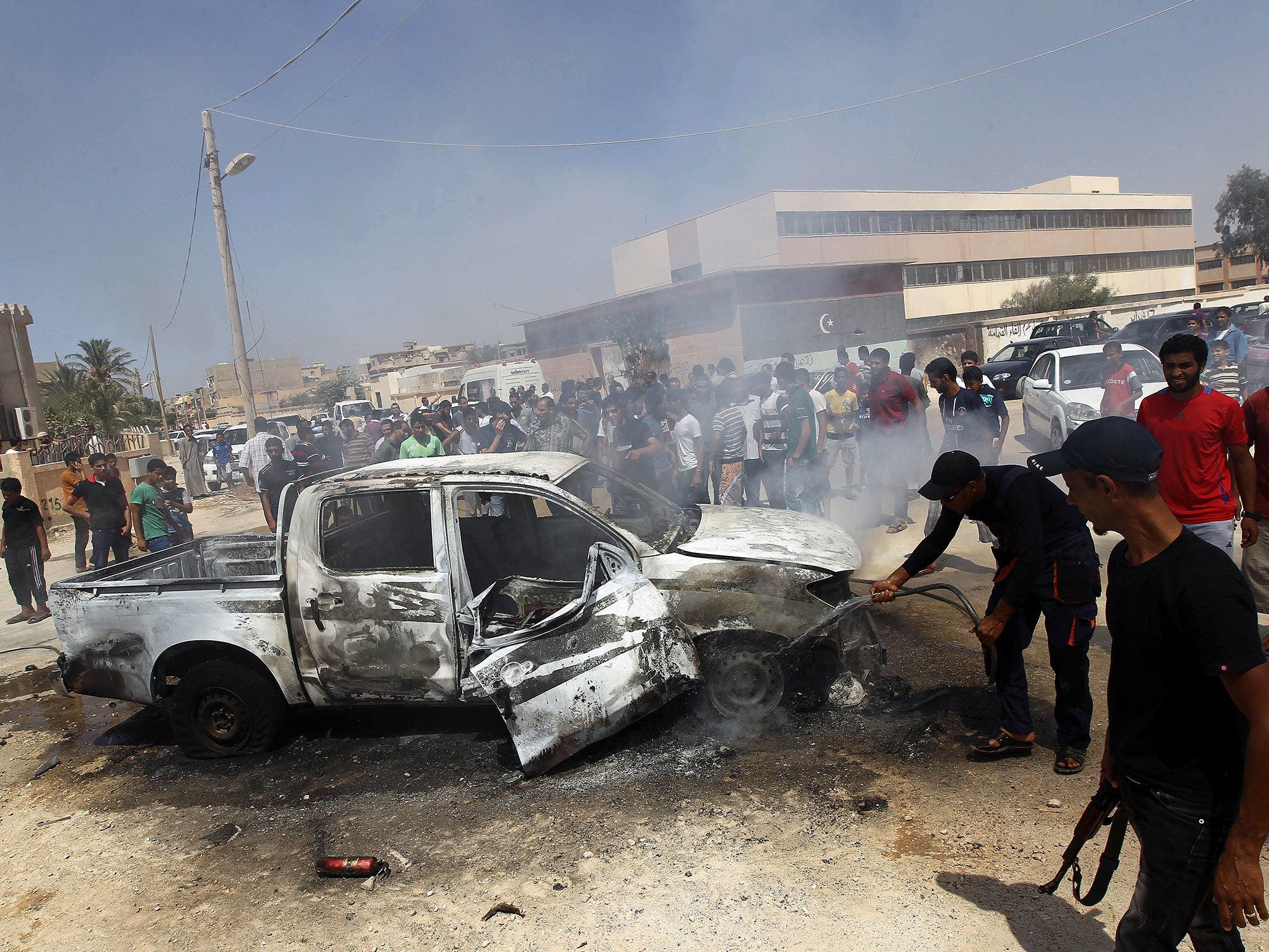 Benghazi residents and Libyan security forces gather around a burning car after an explosion killed the military prosecutor for Western Libya Youssef Ali al-Asseifar on 29 August, 2013