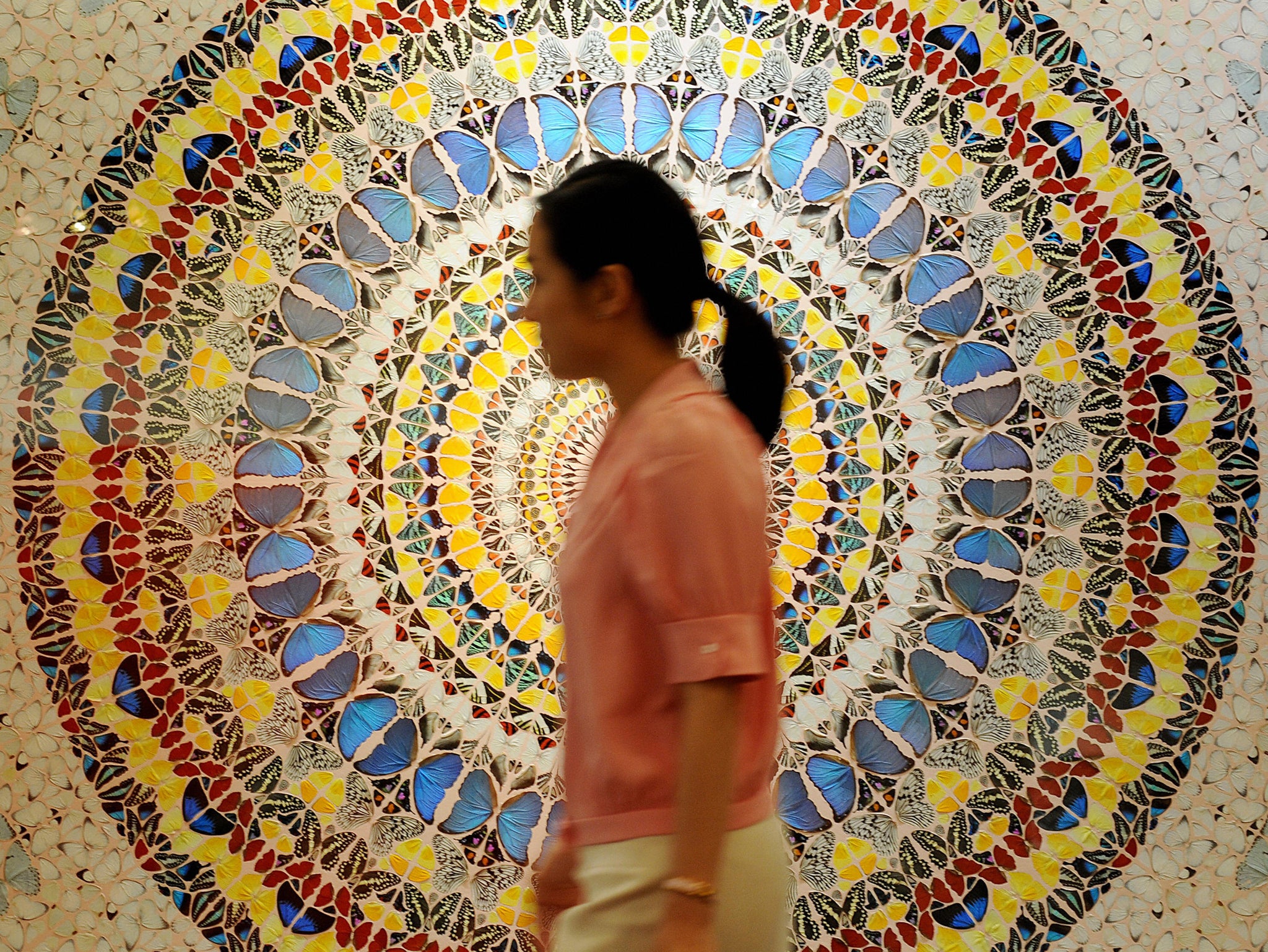 A woman walks past 'Tranquility' by artist Damien Hirst made up of butterfly wings and household gloss on canvas at an exhibition in Hong Kong