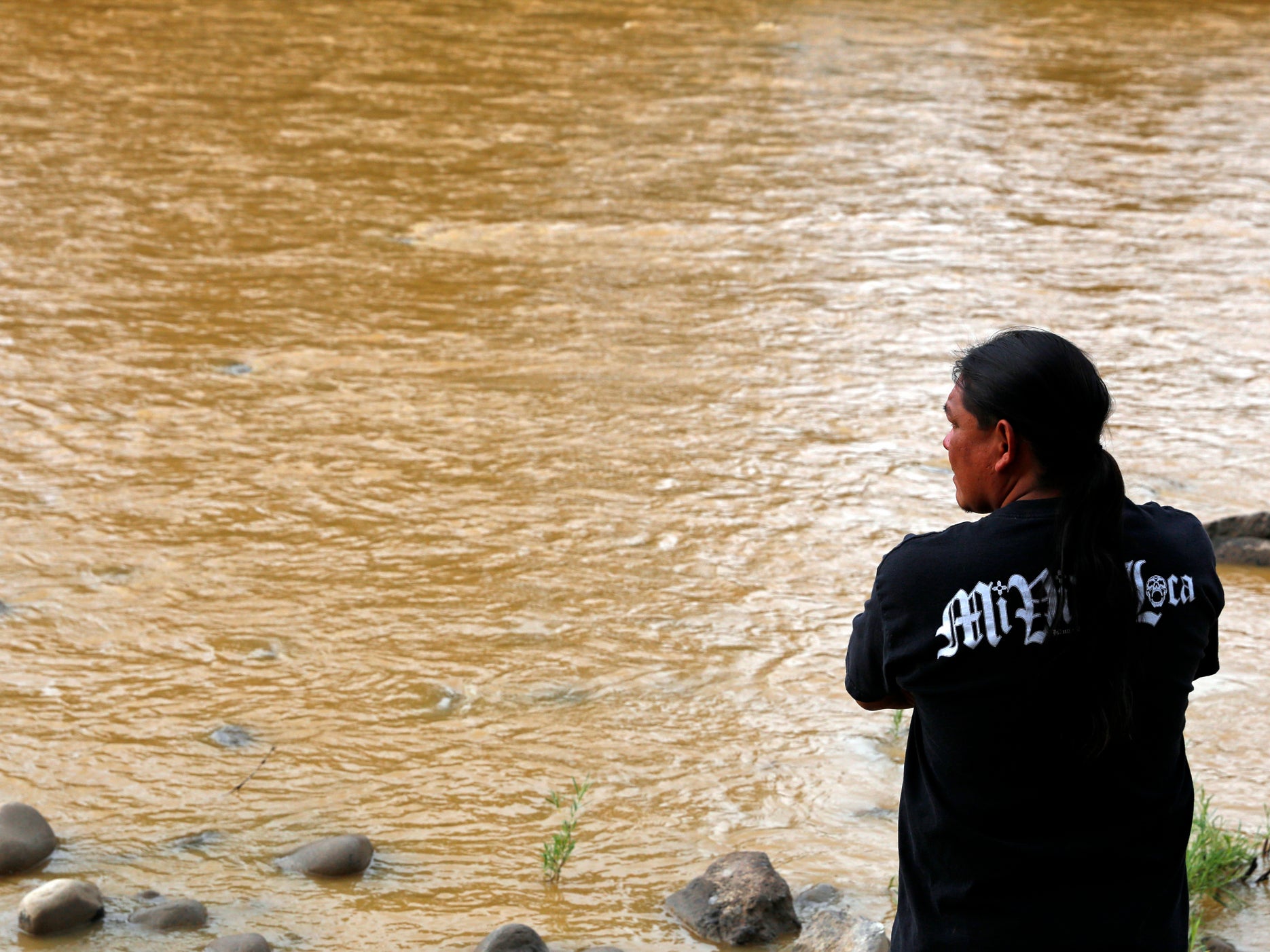 Travis Sells, of Farmington, N.M., looks at the orange sludge from a mine spill upstream flowing past Berg Park in Farmington.