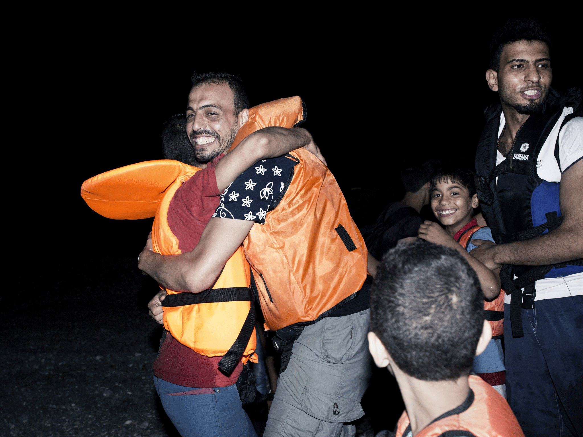 Migrants hug one another after getting out of an inflatable boat on a beach on the Greek island of Kos