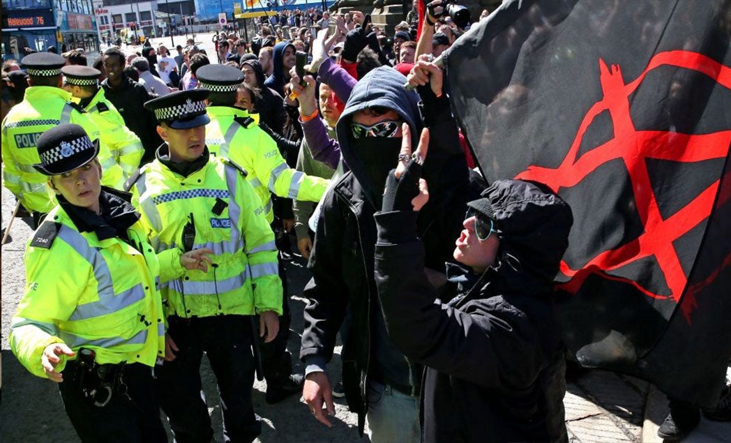 A woman holding an anarchist flag gestures as police intervene in Liverpool to protect members of National Action as it cancelled its "White Man March"