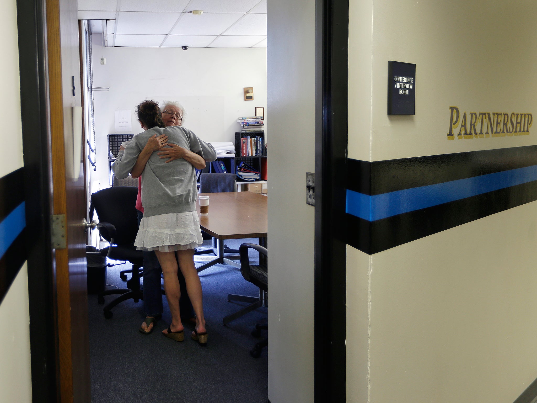 Volunteer Ruth Cote, facing, hugs a woman inside the police station in Gloucester