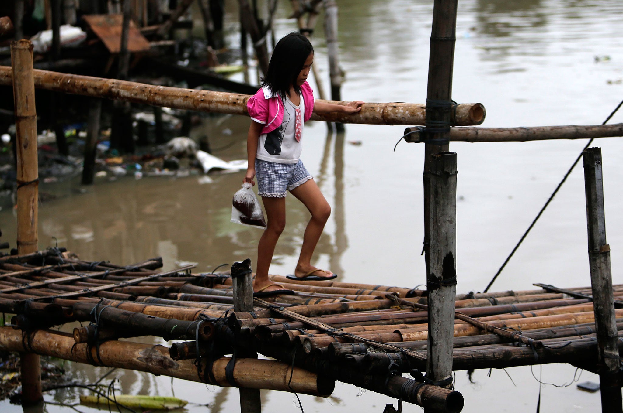 A Filipino girl maneuvers on a makeshift bridge at a swelling river in Las Pinas city, south of Manila, Philippines