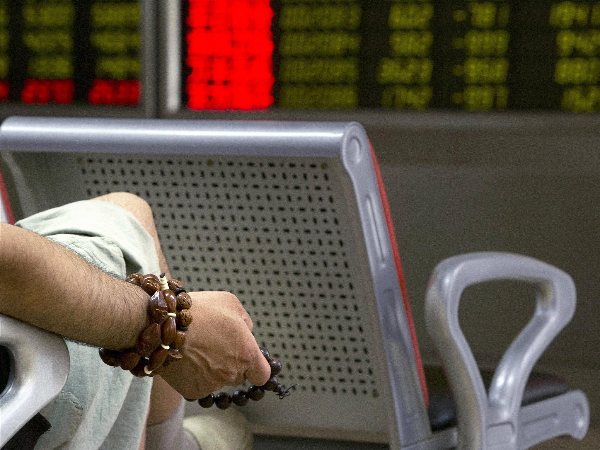 A Chinese investor holds prayer beads as he monitors stock prices at a brokerage house in Beijing