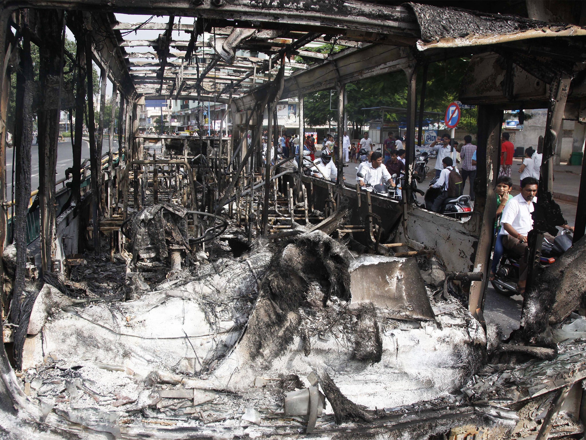 Indian commuters pass by a damaged bus which was set on fire during clashes in Ahmadabad, India