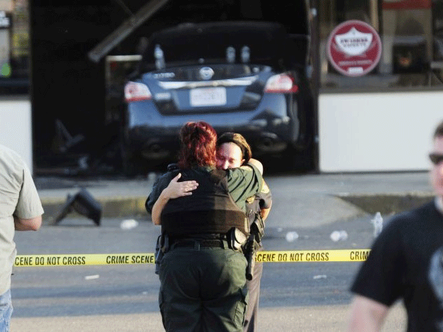 A Sunset police officer and another law enforcement officer embrace in front of the Sunset Mini Mart