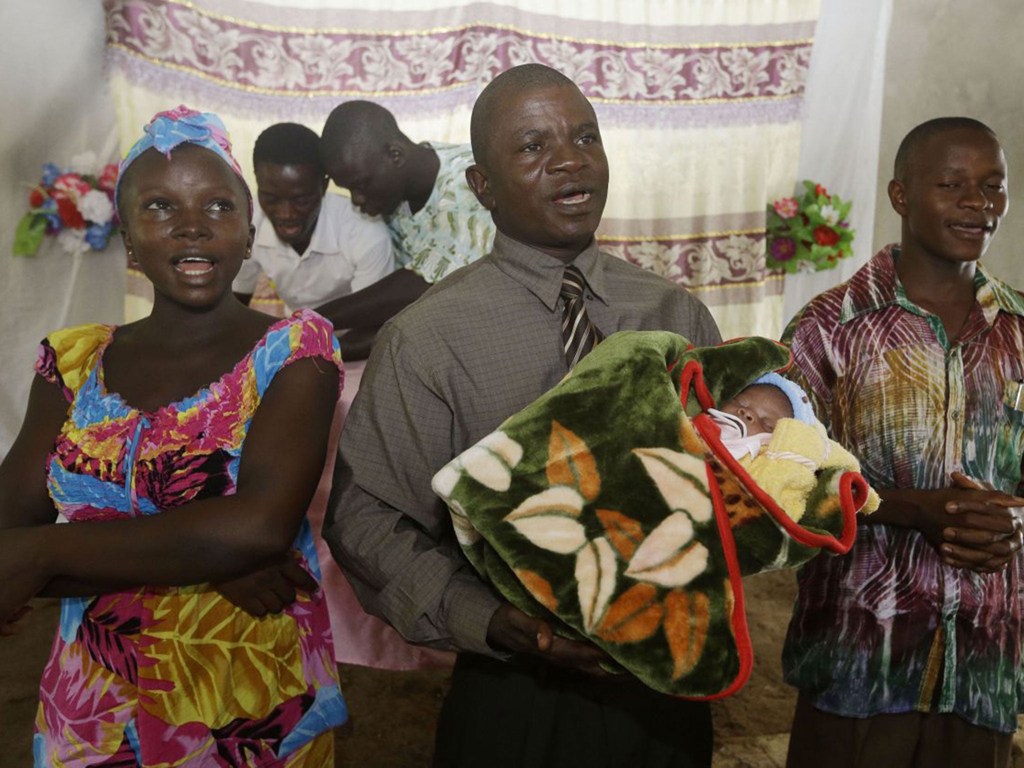 Ebola survivor Victoria Yillia, left, Pastor Gabriel Abu, center, holding Yillia's newborn son Barnabas and Anthony Yillia, right, sing before prayers during a church service in Kenema