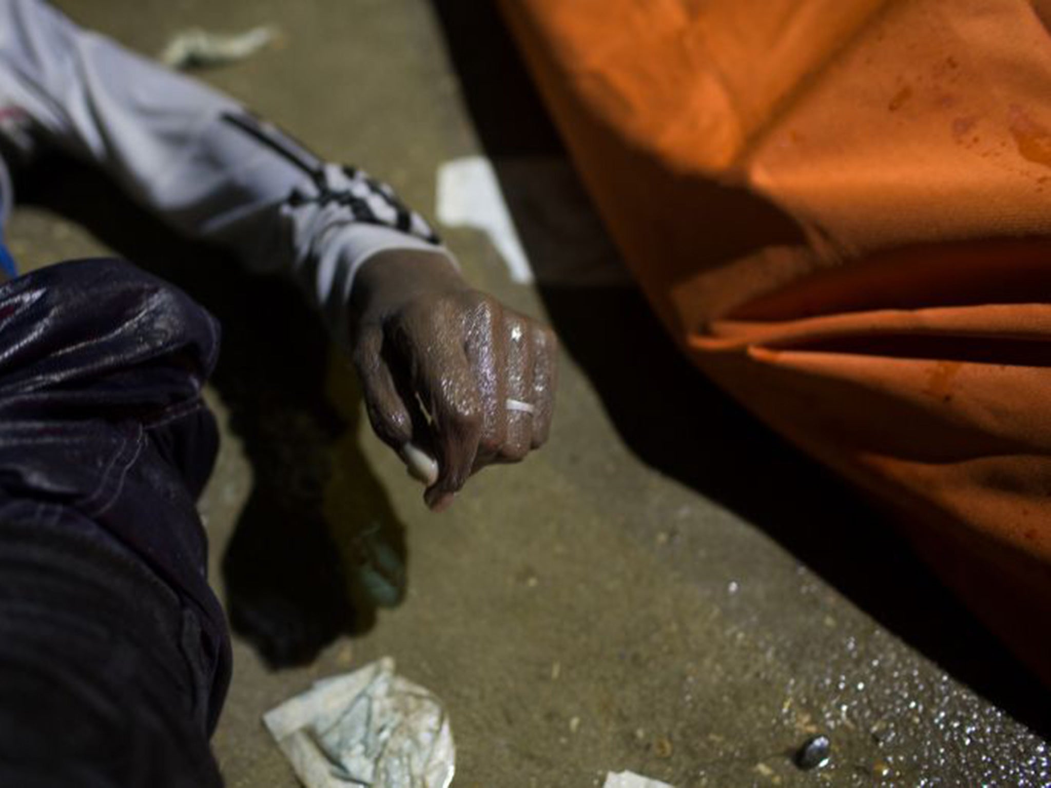 The body of a drowned migrant wearing a wedding ring lies on a dock in Zuwara, Libya, after his boat sank off the coast on Thursday