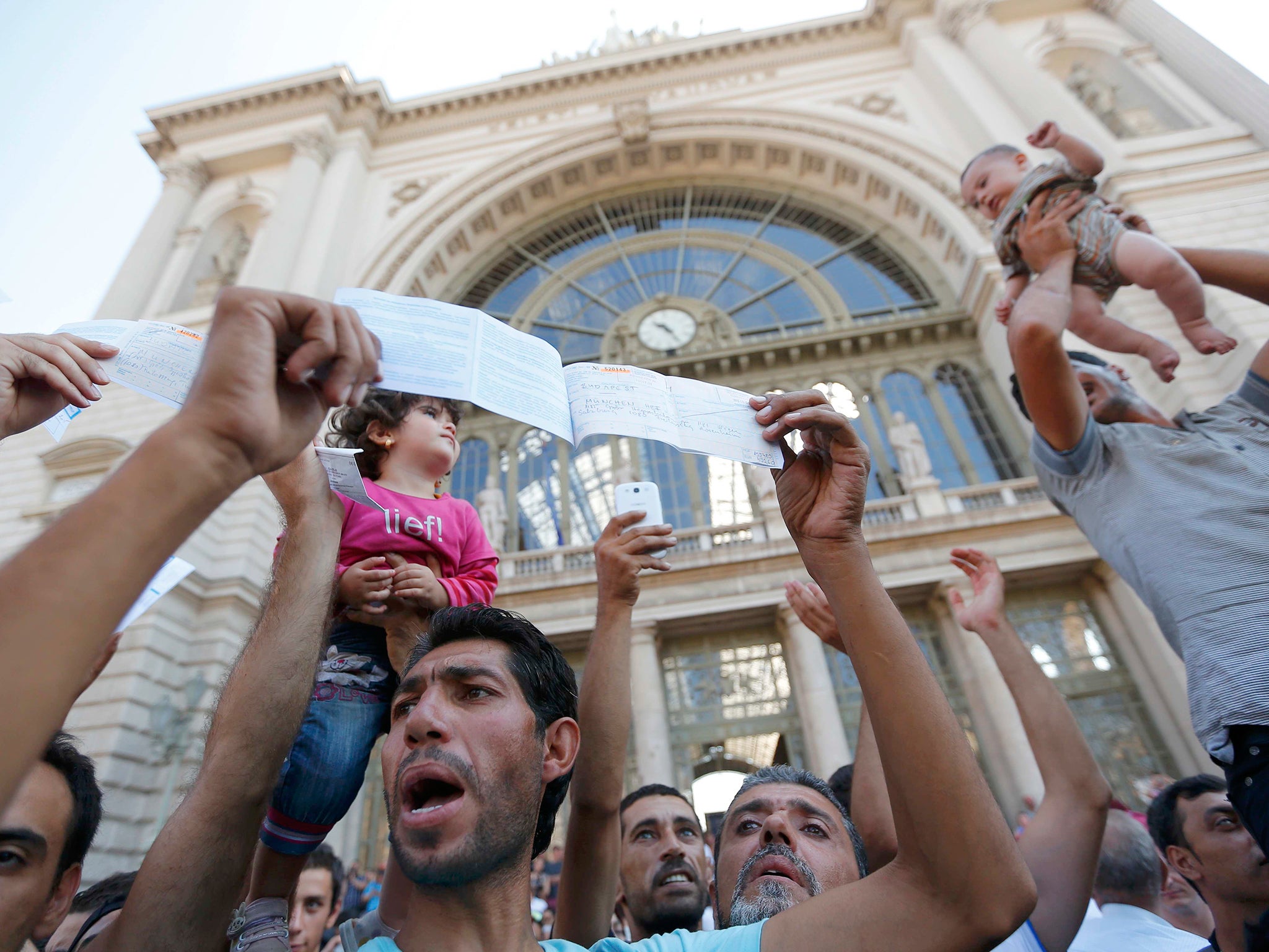 Migrants wave their train tickets and lift up children outside the main Eastern Railway station